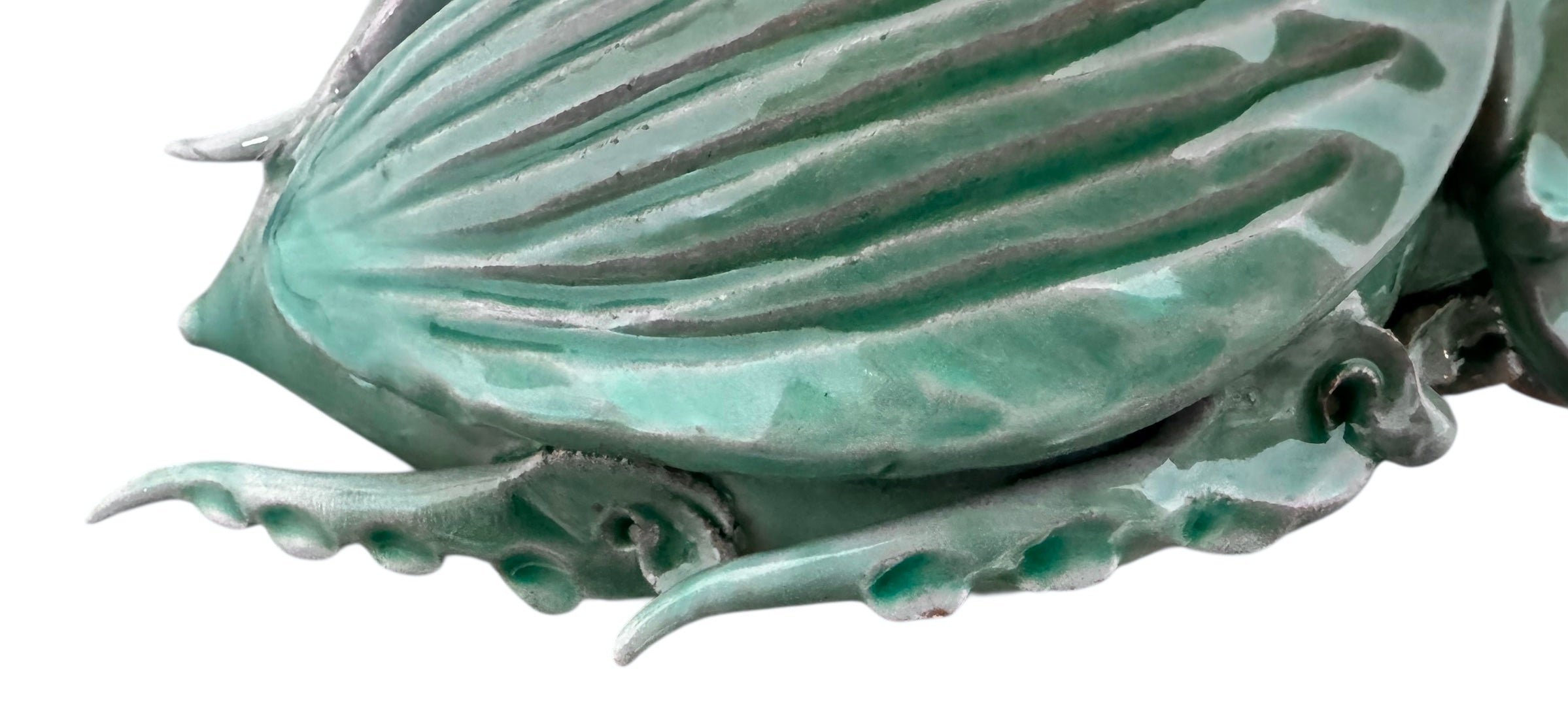 A ceramic sculpture of a stylized beetle by Enza Fasano, featuring a deep emerald green glaze with dark, metallic bronze-colored accents. The beetle is depicted with a highly textured, ribbed shell (elytra) and prominent, curved horns. Its legs are stylized with suckers, reminiscent of octopus tentacles. The piece has a glossy finish and rests against a plain white background.