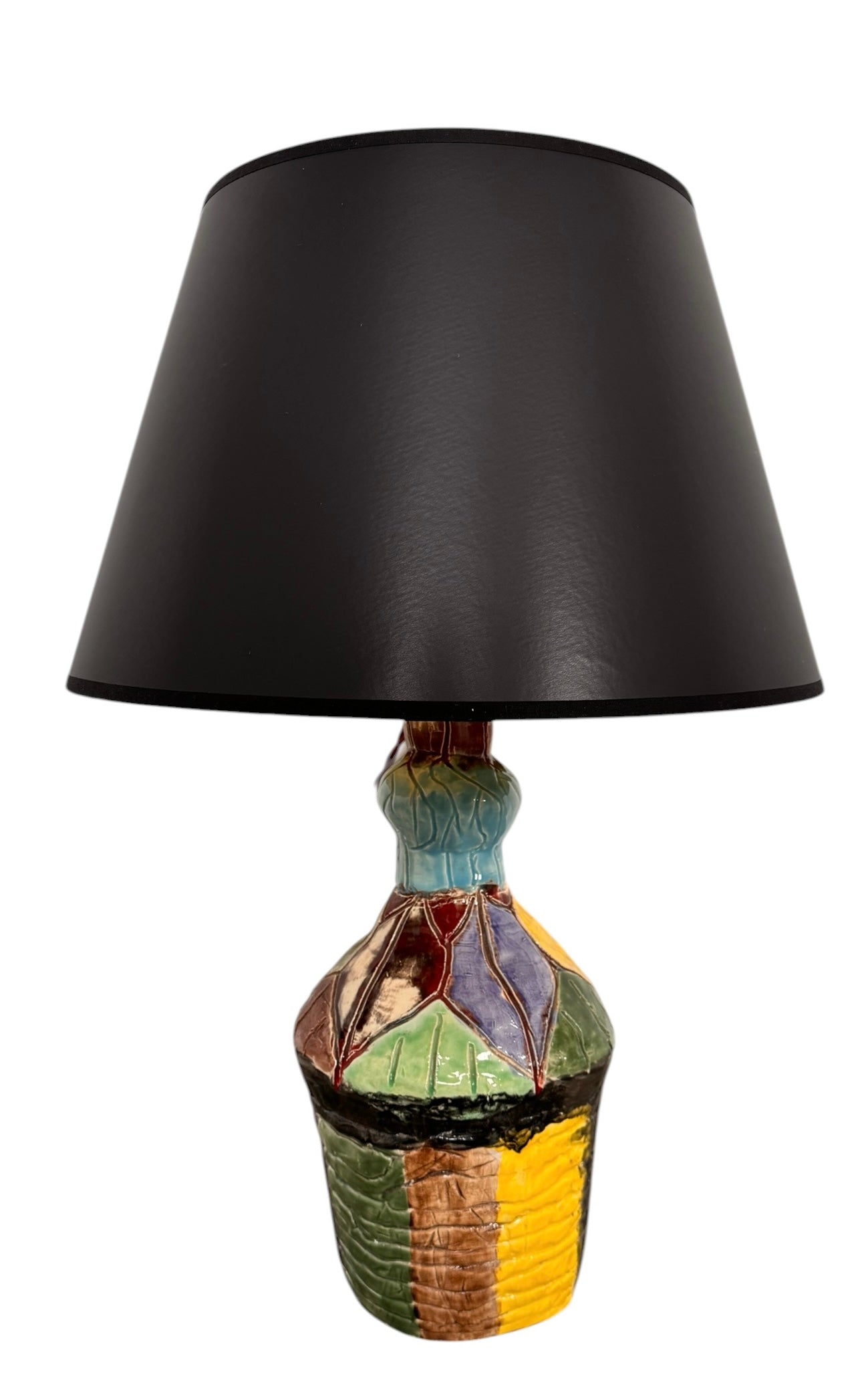 A hand-crafted ceramic table lamp featuring a vibrant, multi-colored base and a sleek black shade. The base is an upcycled artisan vase with a textured, hand-thrown appearance, decorated with geometric panels in shades of mustard yellow, forest green, cobalt blue, and burgundy, separated by thick black outlines. The lamp is topped with a minimalist, black tapered drum shade that provides a sharp contrast to the colorful, eclectic pottery below.