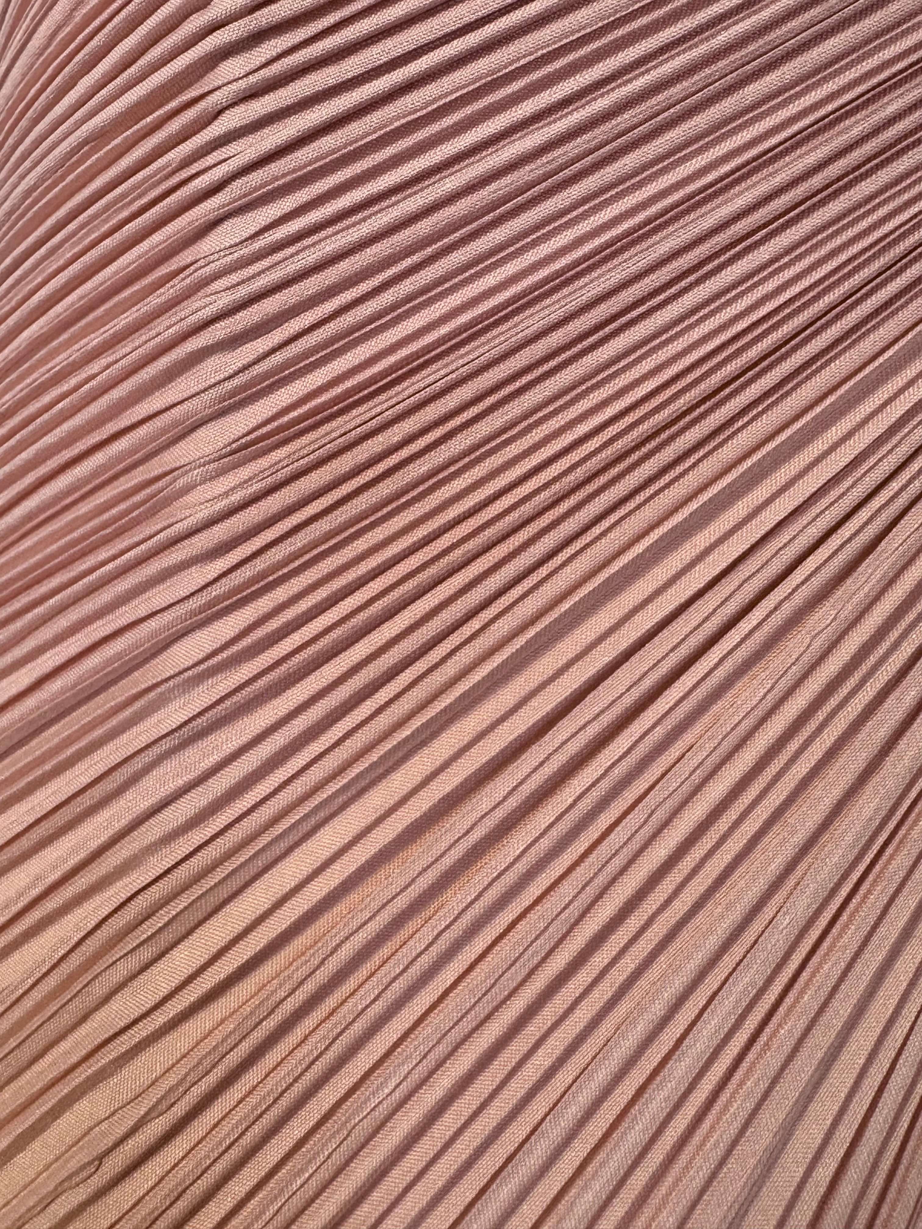 A table lamp featuring a teardrop-shaped, reddish-purple glass base and a conical, pleated, light-pink fabric shade.