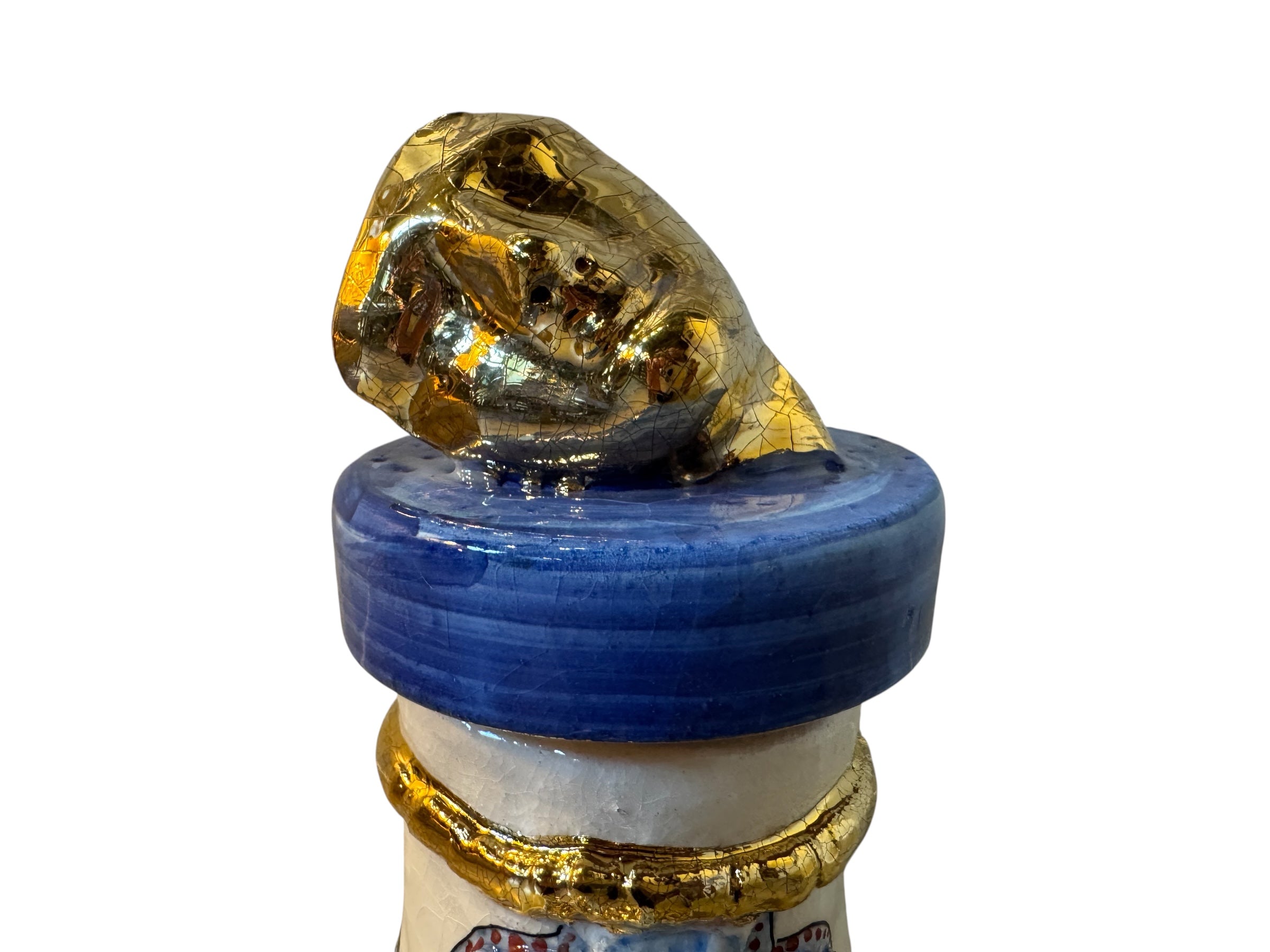 Close-up of a ceramic foot sculpture by Domenico Pinto. The foot is decorated with intricate hand-painted designs inspired by Apulian folklore and accented with 24KT gold. A stylized gilt mask sits atop the foot.