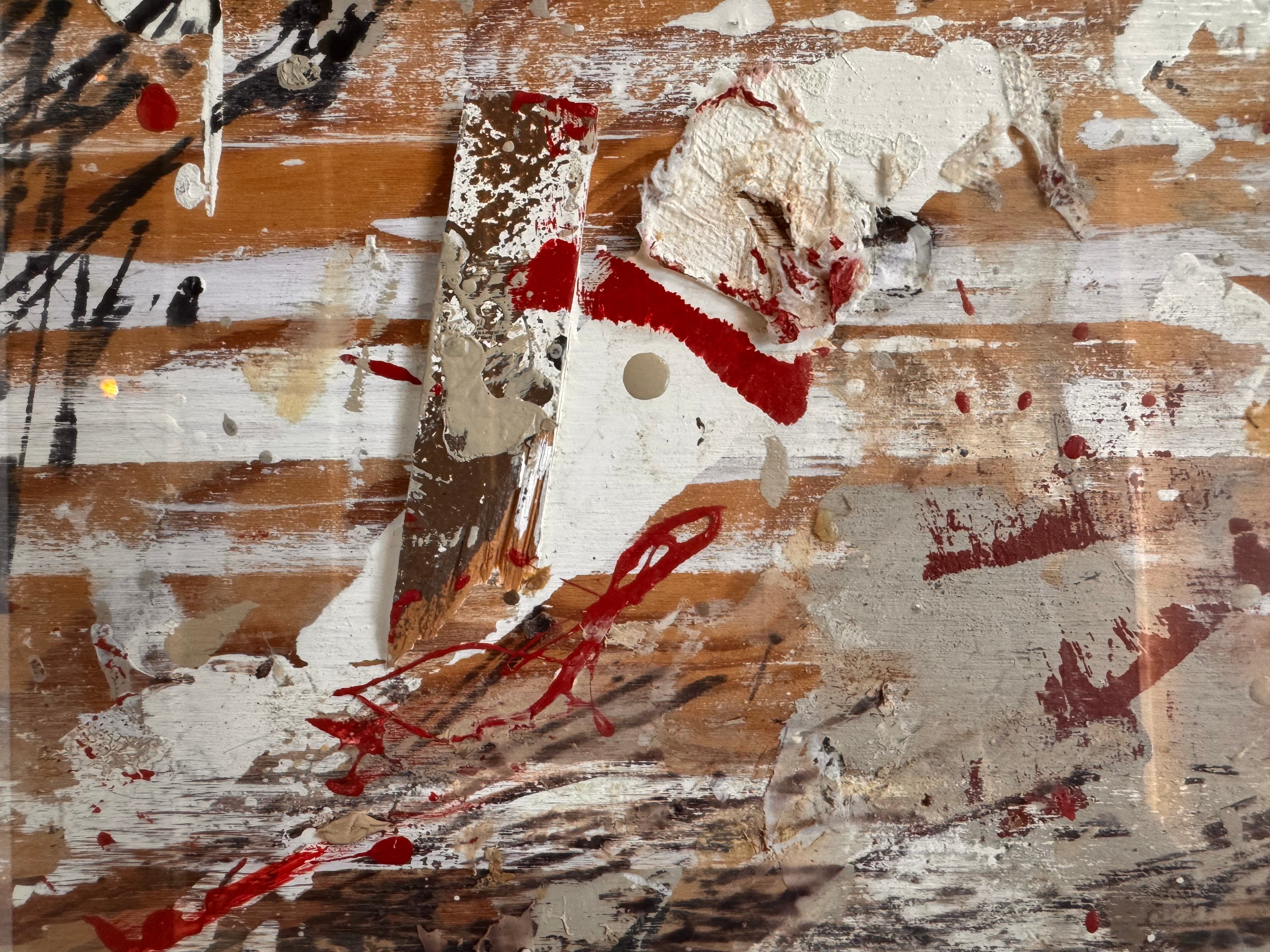 horizontal rectangular mixed media abstract artwork by J. Rogers, dated 2010, presented in a thin black frame. The composition is set against a light-toned wood grain background and features a dynamic, gestural arrangement of thick white impasto, splatters of red and black paint, and aggressive black scribbles. A vertical strip of textured material is collaged near the center, while various washes of tan and cream create a sense of weathered depth across the wooden surface.