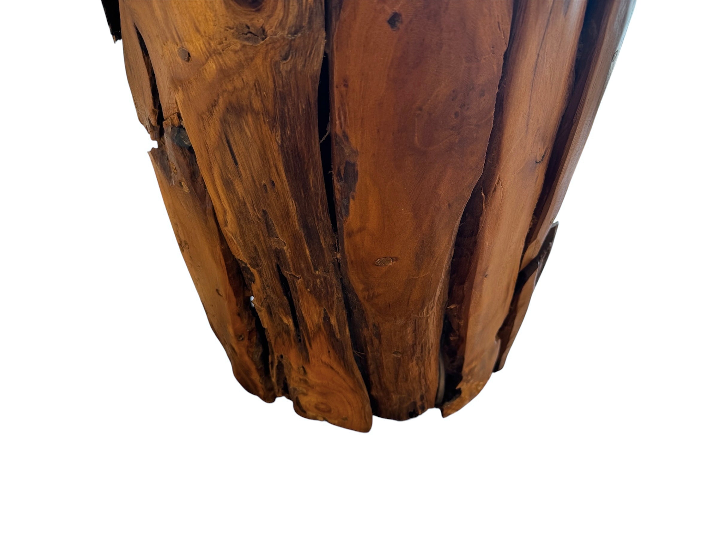 Two table lamps made from repurposed teak wood vases. The bases are tall and tapered, featuring a rugged, mosaic-like texture composed of various pieces of dark, polished teak wood with visible natural grain and crevices. Each lamp is topped with a large, warm-toned conical shade that is currently wrapped in protective clear plastic, emitting a soft, golden glow. The lamps are positioned on a clean white surface against a neutral background.
