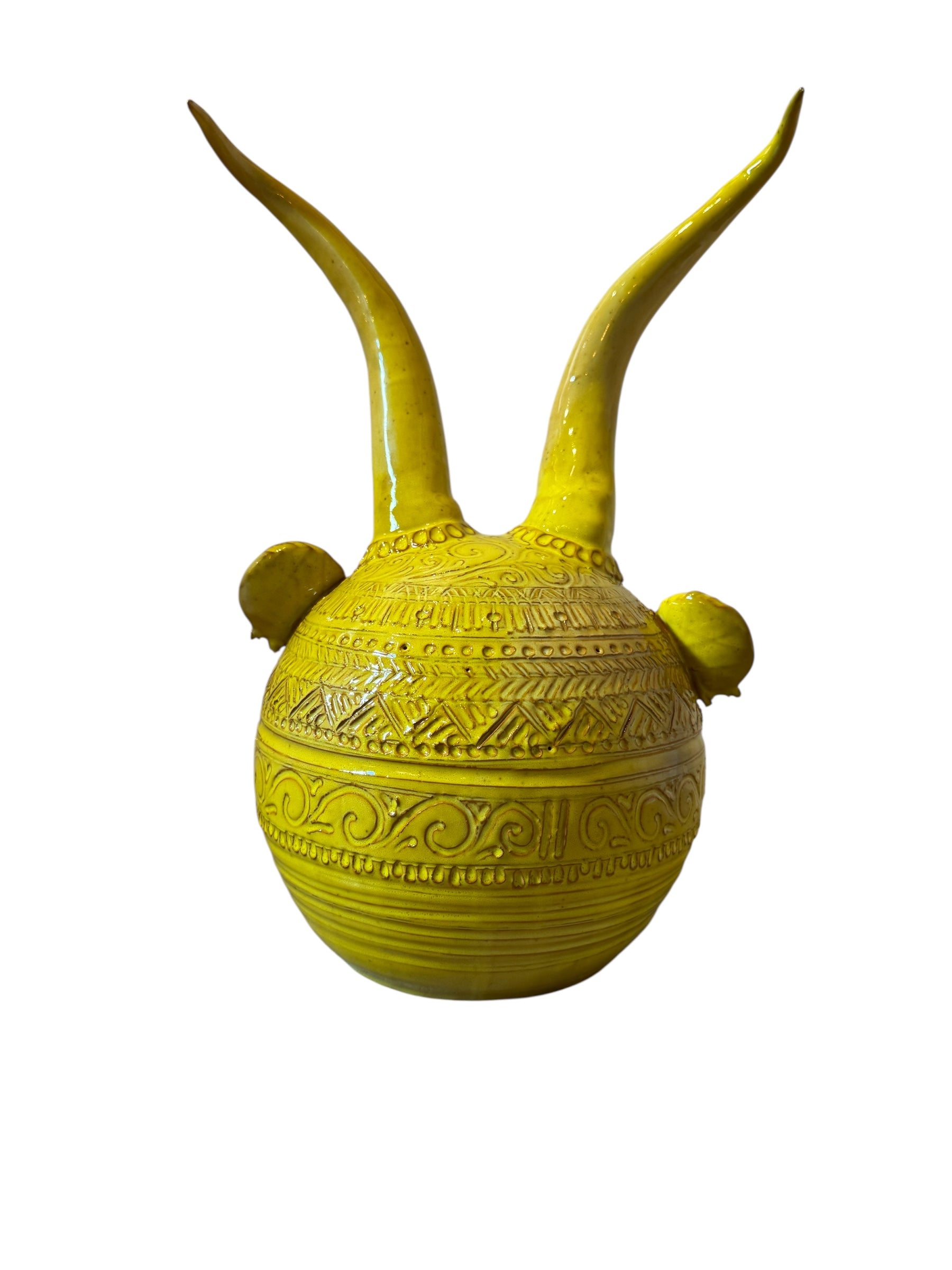 Yellow ceramic sculpture titled 'The Ram Oracle' by Enza Fasano, featuring a round body with intricate, hand-incised patterns and long, stylized ram-like horns