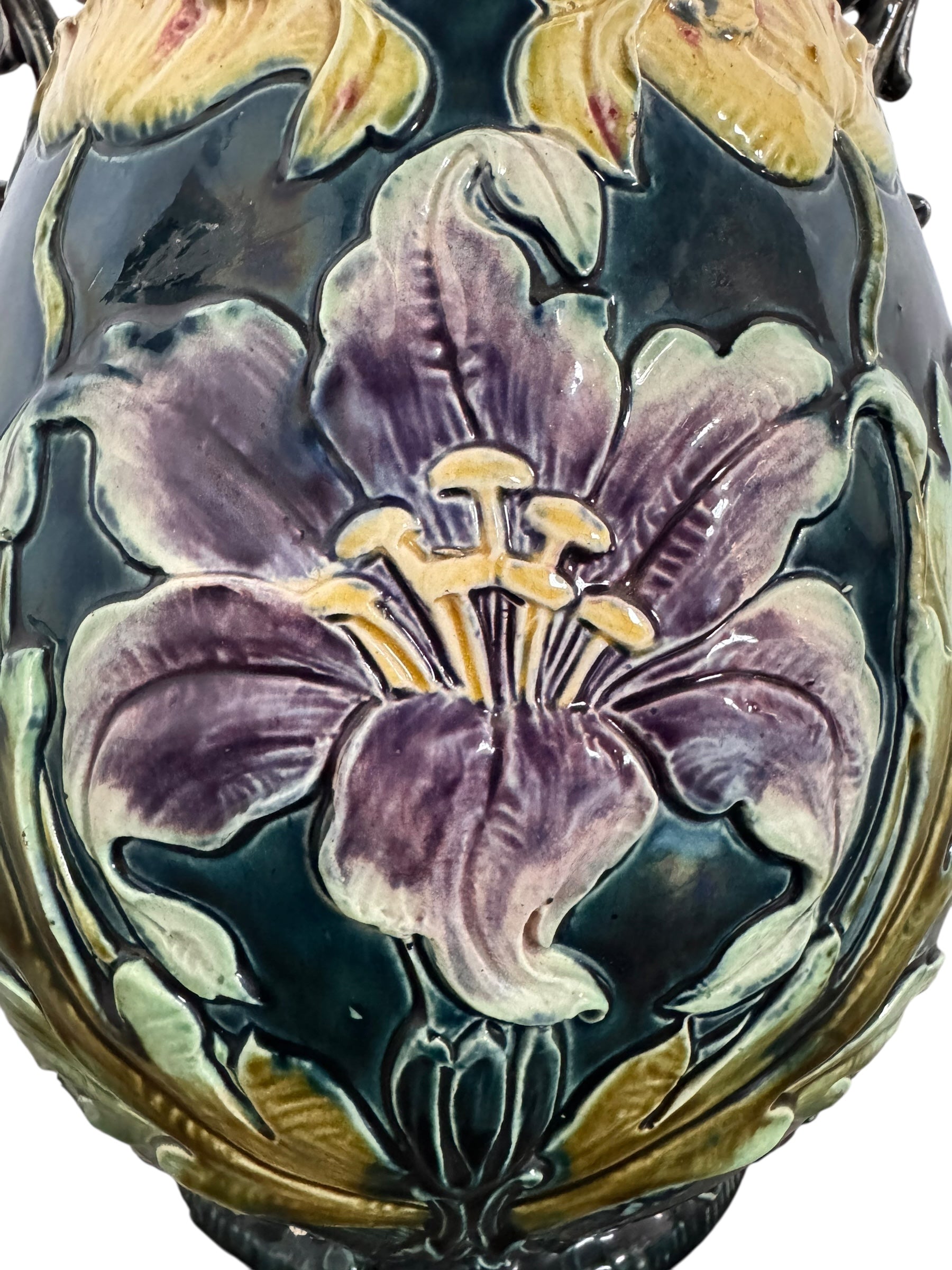 An ornate, dark glazed ceramic Art Nouveau vase with two handles and raised floral designs in yellow, purple, and green.