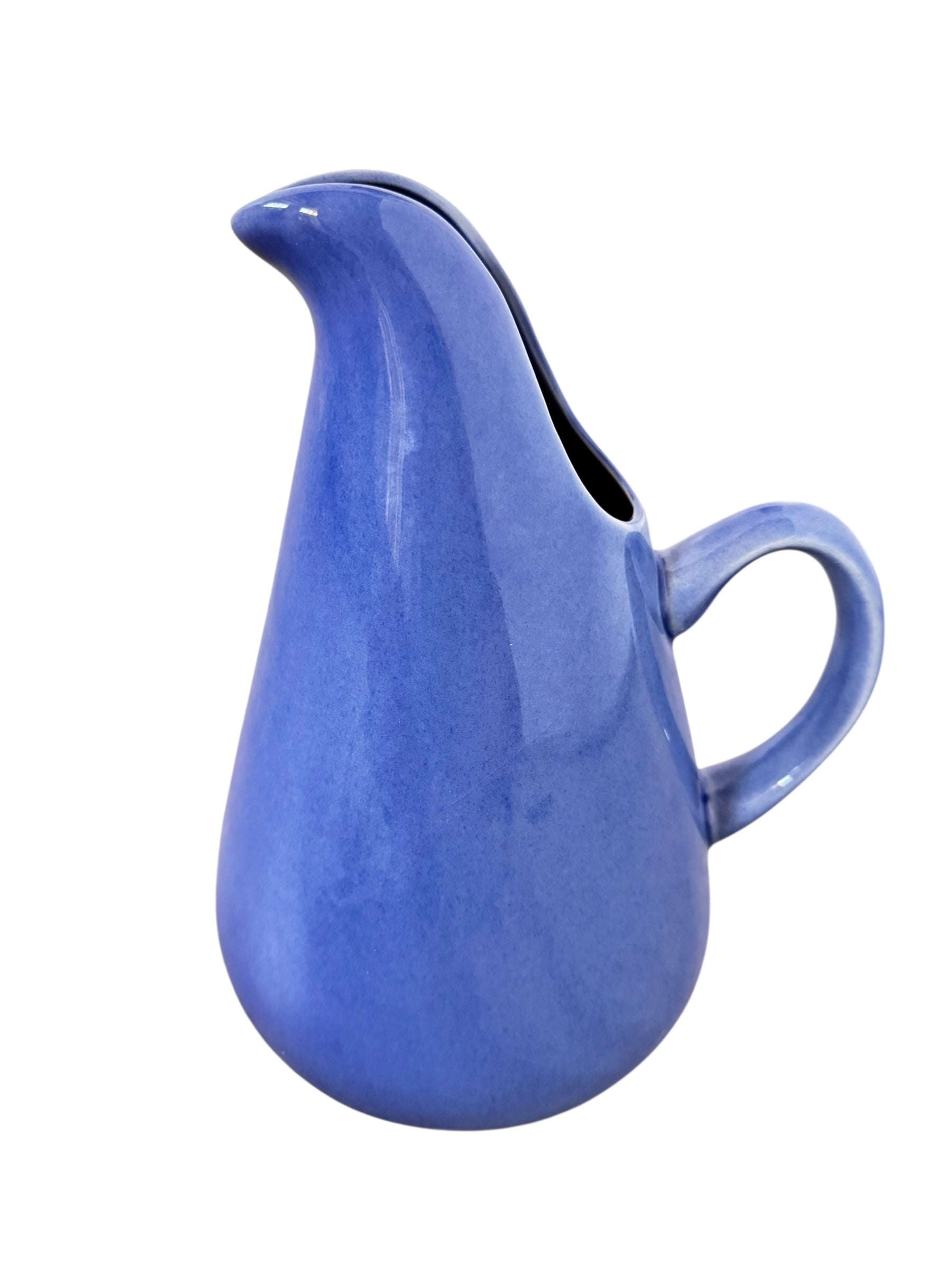 A Russel Wright American Modern stoneware water pitcher in a glossy Manitoga blue glaze is centered against a white background. The pitcher has a teardrop shape, a large handle, and a wide spout