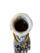 Handcrafted ceramic sculpture in the shape of a foot, decorated with intricate black and white patterns, 24KT gold accents, and topped with a blue lid featuring a gilt fish and head emerging from stylized waves.