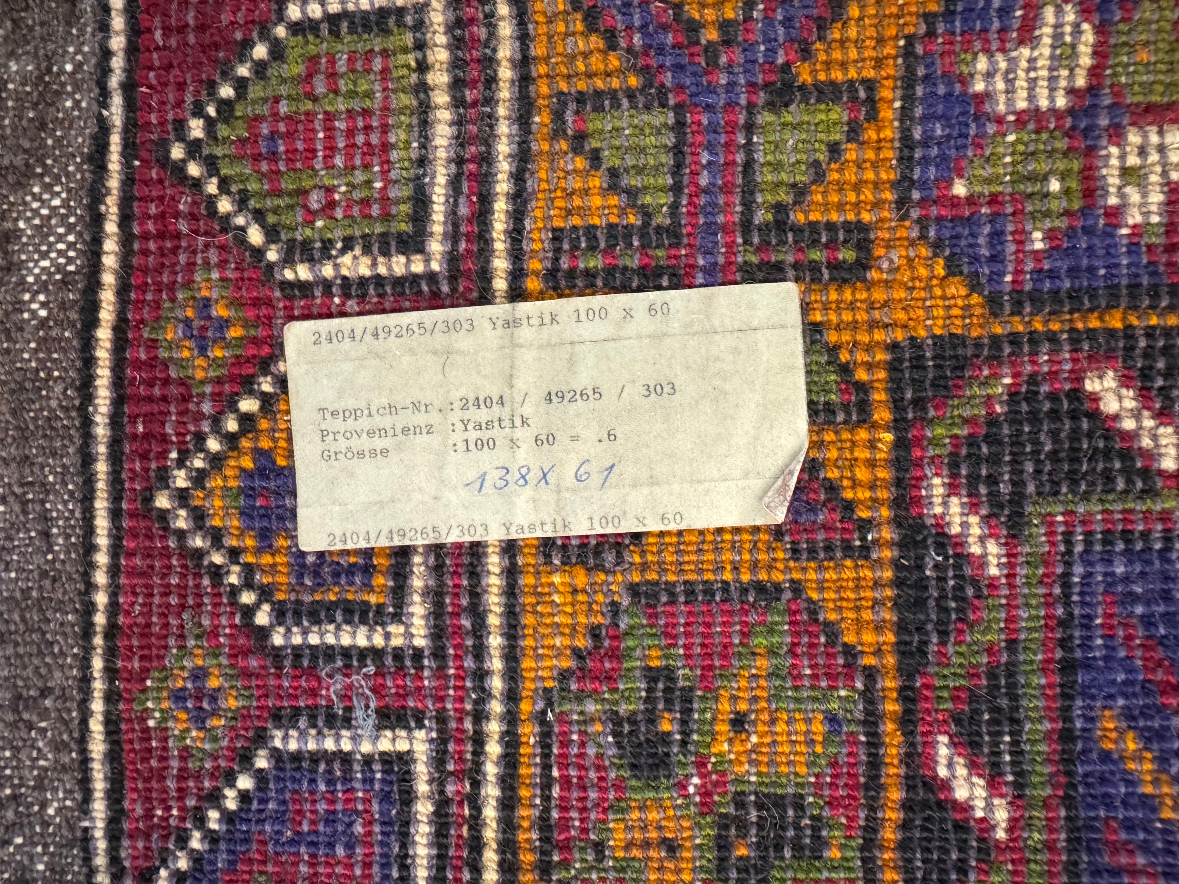 A close-up view of a hand knotted Yastik rug with a label indicating the product name and dimensions.