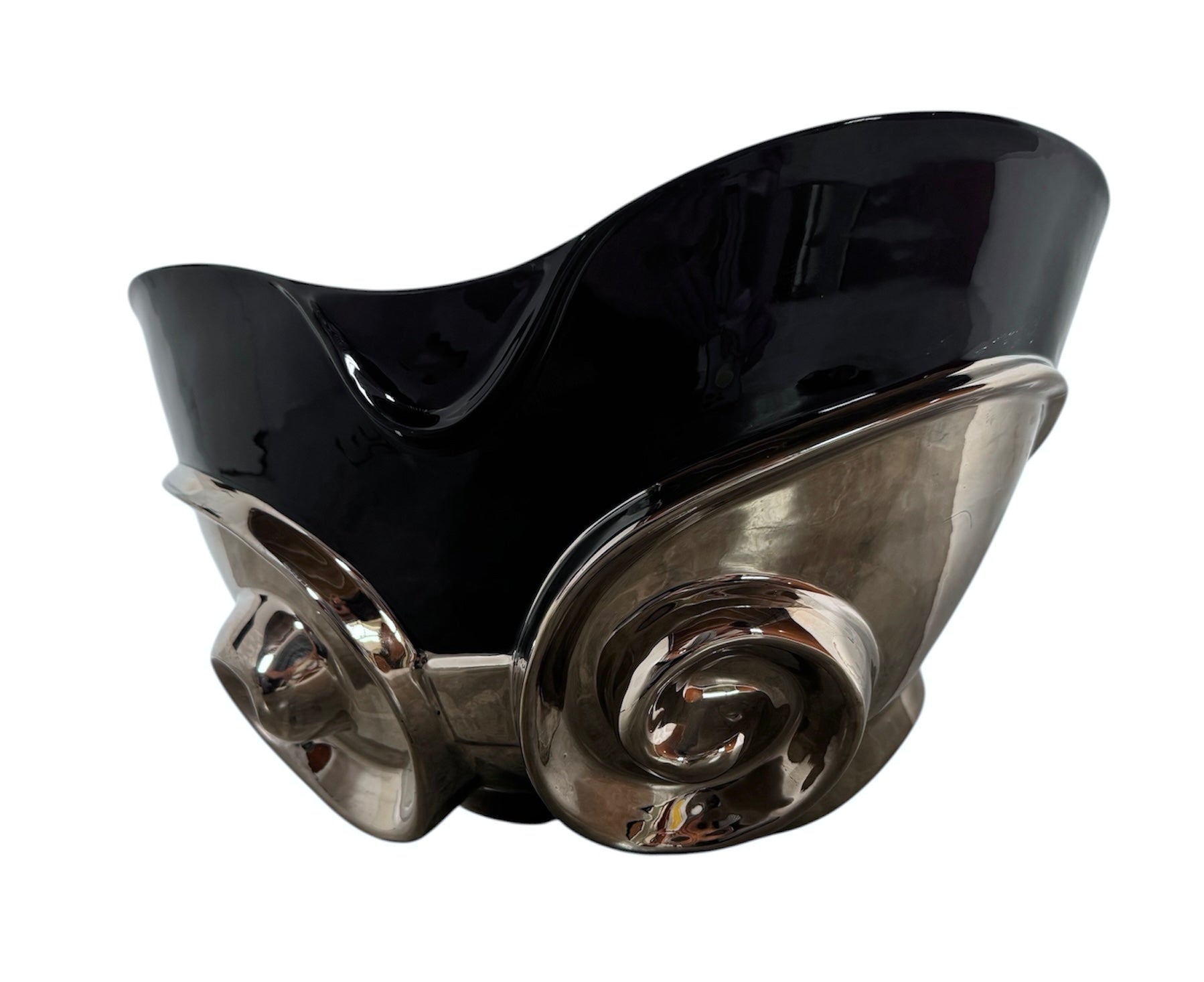 A large, decorative ceramic bowl by Dolbi Cashier in a dramatic Postmodern style. The top half is finished in a polished, piano-black glaze with an organic, wavy "butterfly" rim that dips in the center and rises at the sides. The bottom half is finished in a reflective, metallic silver chrome glaze, featuring bold, geometric-rounded feet and a structured base that appears to "hold" the black vessel. The overall shape is wide and sculptural, reminiscent of 1980s Art Deco Revival.