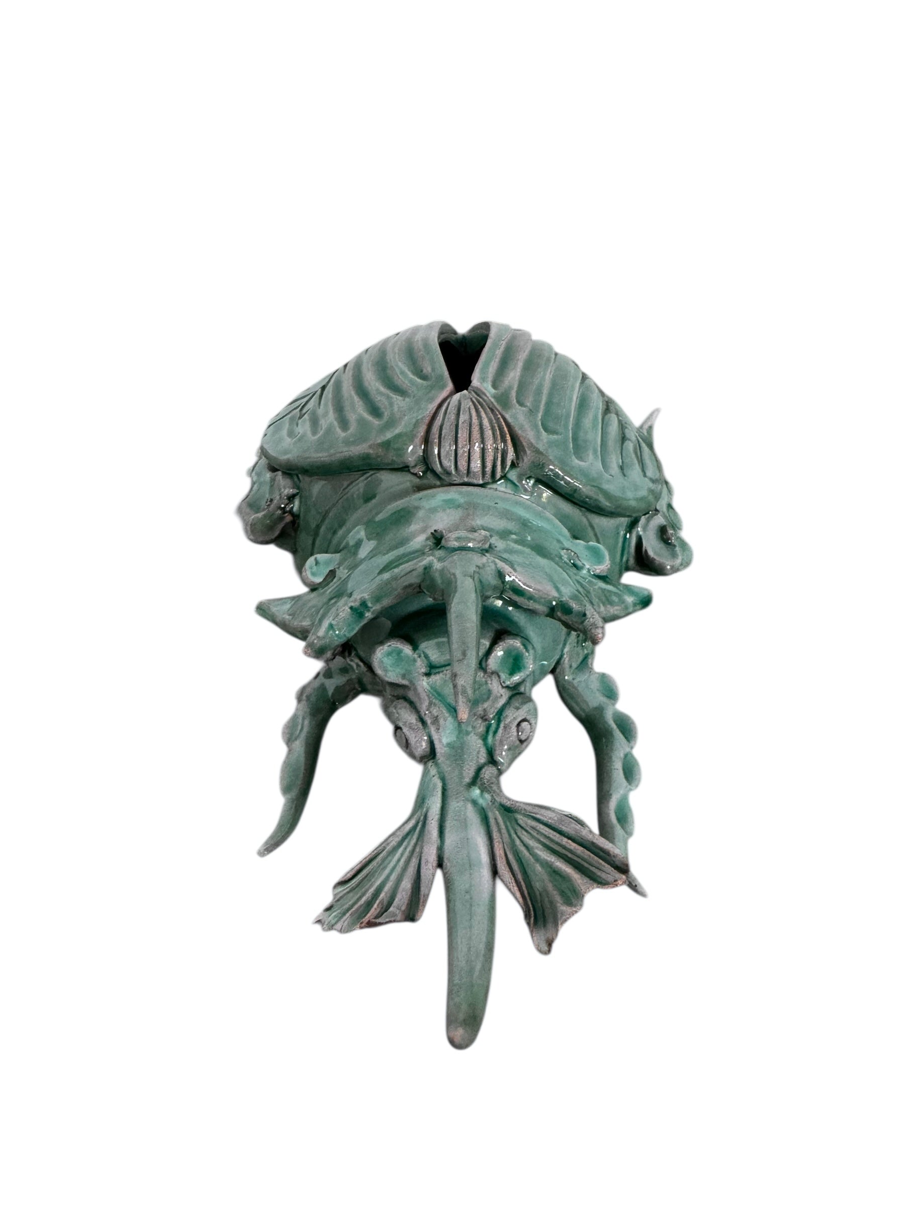 A ceramic sculpture of a stylized beetle by Enza Fasano, featuring a deep emerald green glaze with dark, metallic bronze-colored accents. The beetle is depicted with a highly textured, ribbed shell (elytra) and prominent, curved horns. Its legs are stylized with suckers, reminiscent of octopus tentacles. The piece has a glossy finish and rests against a plain white background.