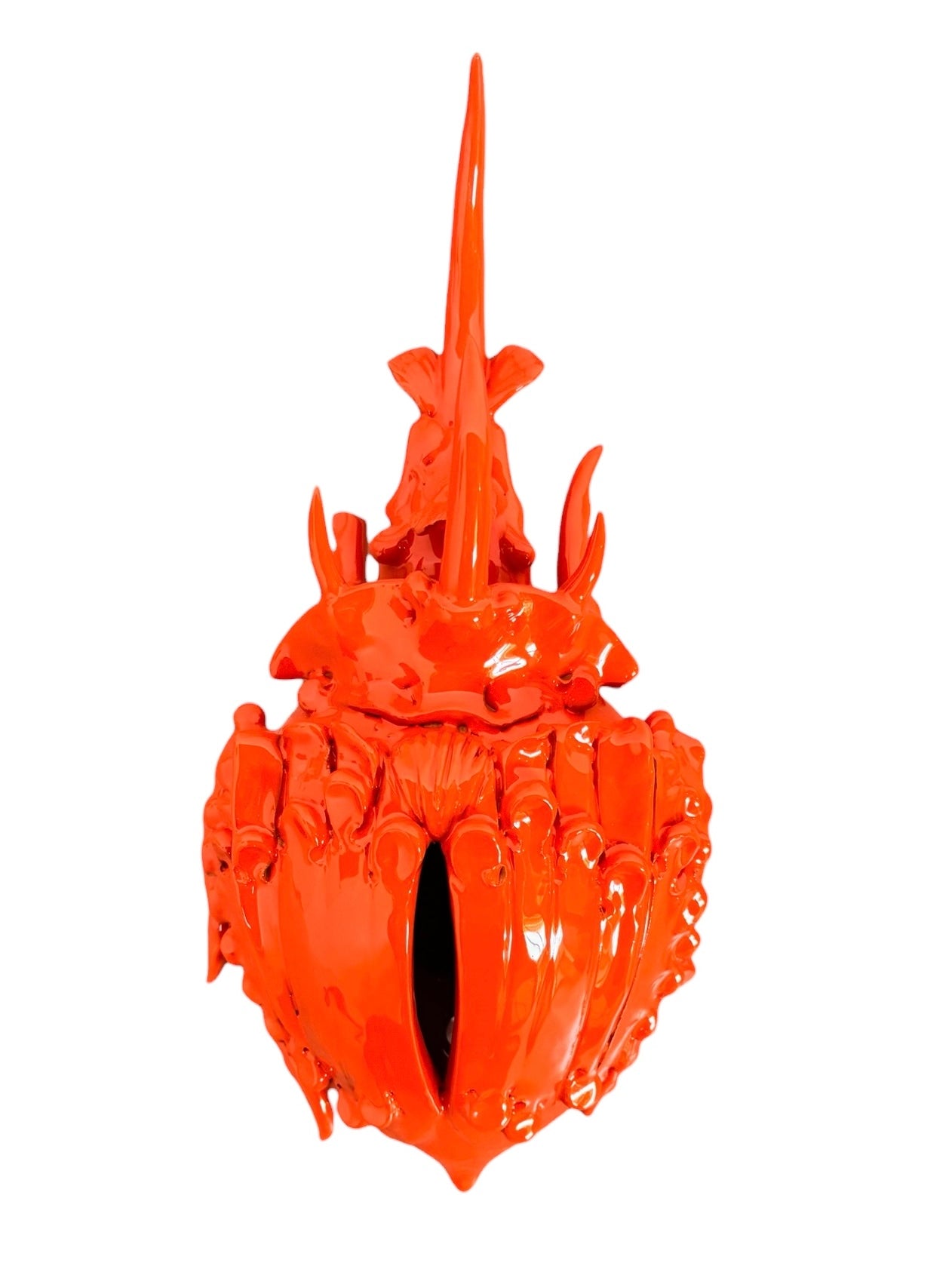 A glossy, vibrant orange ceramic sculpture of a rhinoceros beetle by Enza Fasano. The piece features a highly polished, reflective glaze and stylized, fluid anatomical details. Its prominent dual horns curve forward, and the body is textured with layered, wing-like plates, set against a plain white background.
