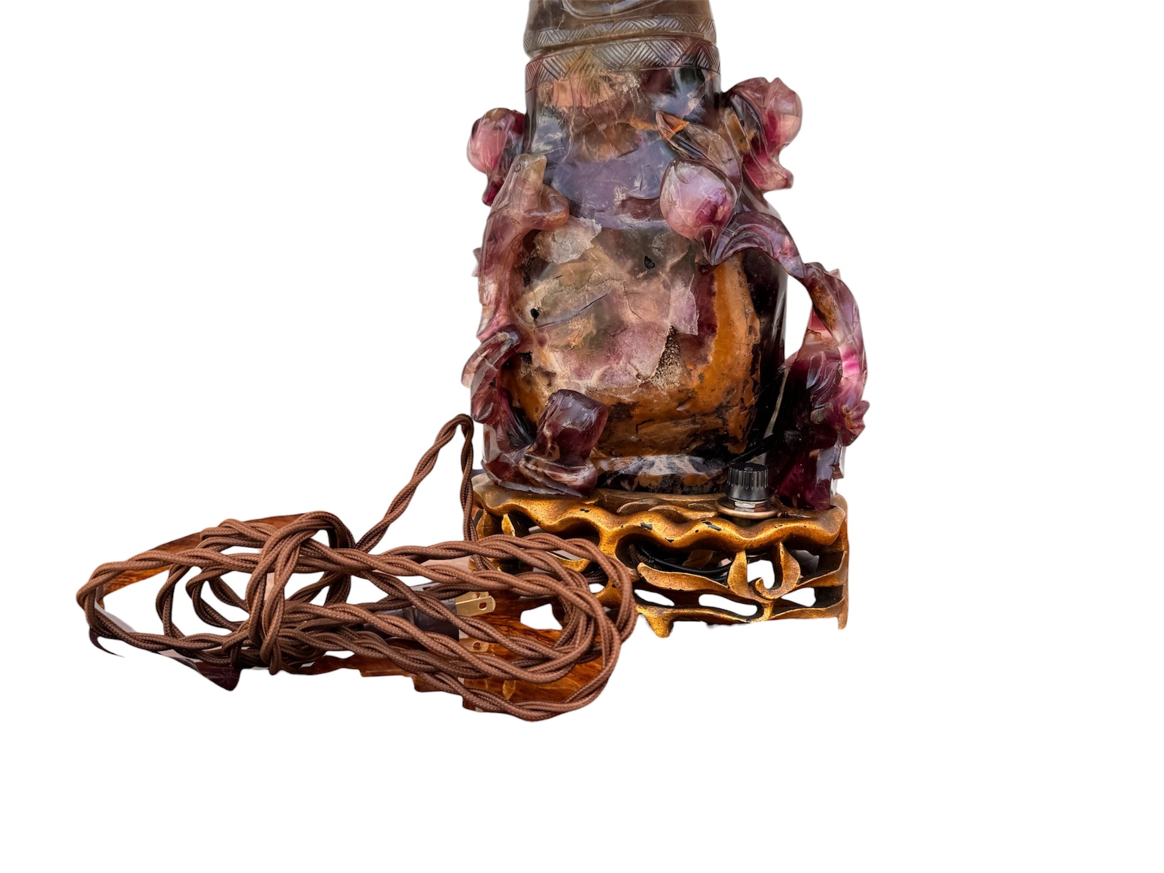 An antique Chinese table lamp featuring a base hand-carved from deep purple amethyst stone, topped with a clear quartz crystal neck. The lamp sits on an ornate, custom gilt-bronze Chinoiserie base and features a flared, cream-colored silk lampshade still enclosed in protective plastic. A rectangular brass finial sits at the very top.