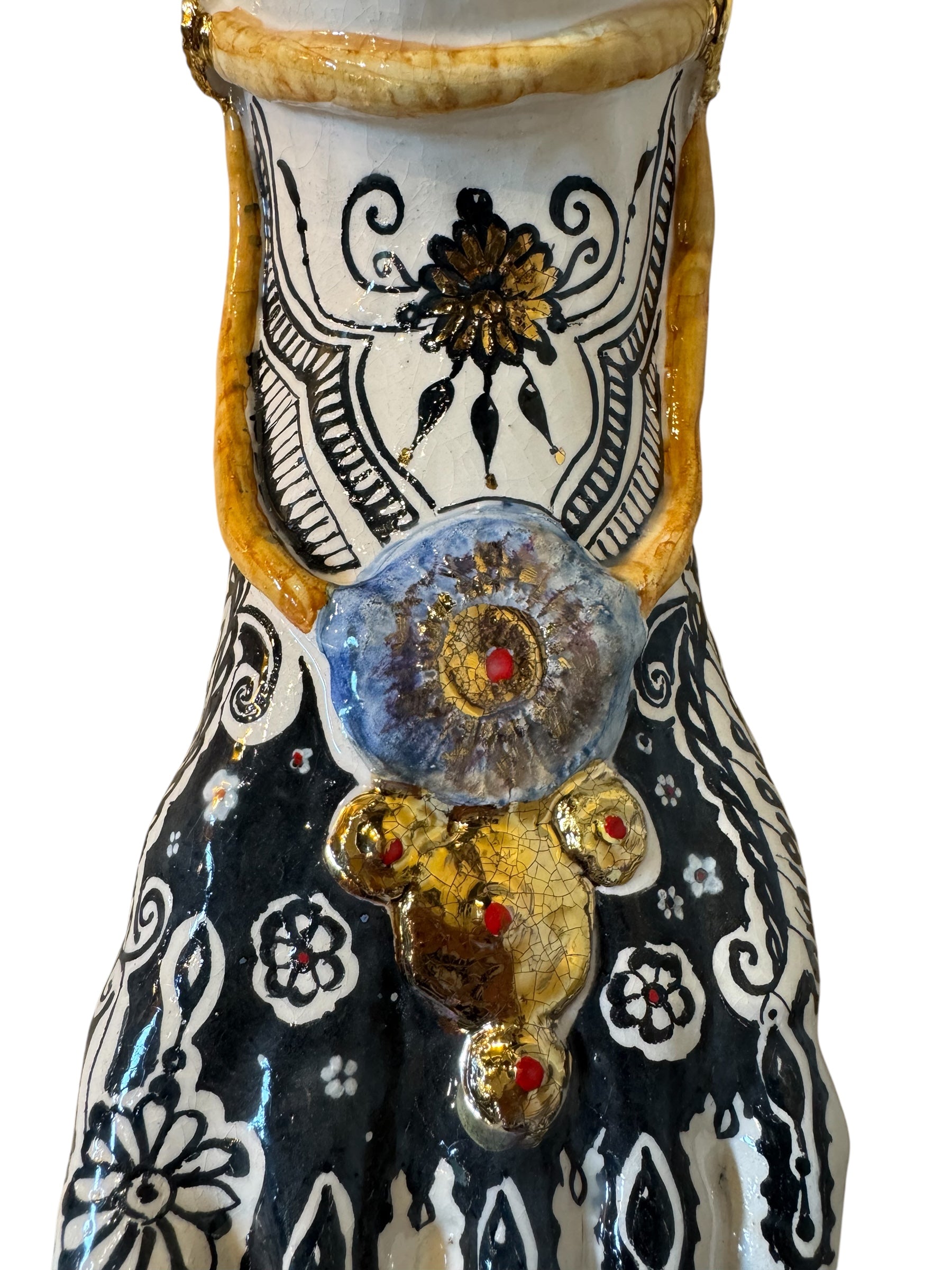 Handcrafted ceramic sculpture in the shape of a foot, decorated with intricate black and white patterns, 24KT gold accents, and topped with a blue lid featuring a gilt fish and head emerging from stylized waves.