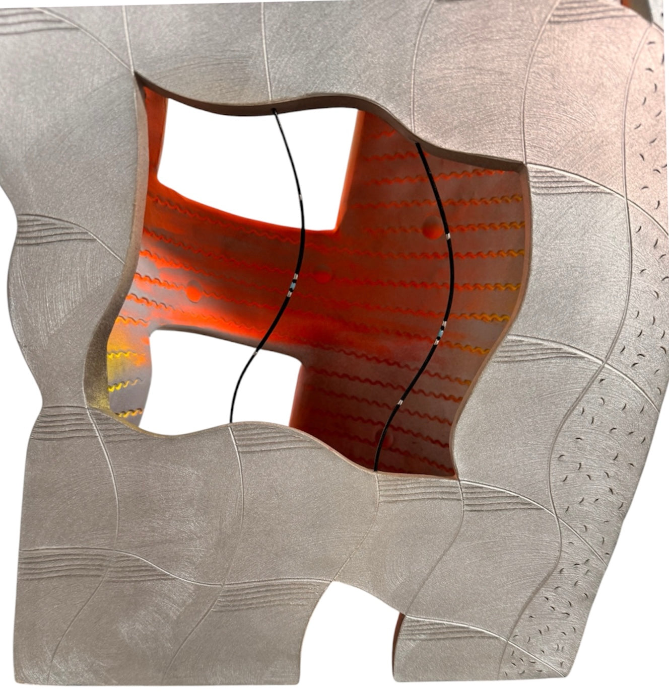 Carved, rib-like vertical lines cover the lower two-thirds of the form, with some sections resembling stacked bricks or tire treads. A subtle metallic silver finish catches the light on the right half, contrasting with the chalky finish on the left. The top third of the sculpture is a smooth, rounded cap. Rectangular cutouts on both sides pierce through the outer layer, revealing a hollow interior glowing with vibrant, airbrushed gradients of neon pink, orange, yellow, and green.