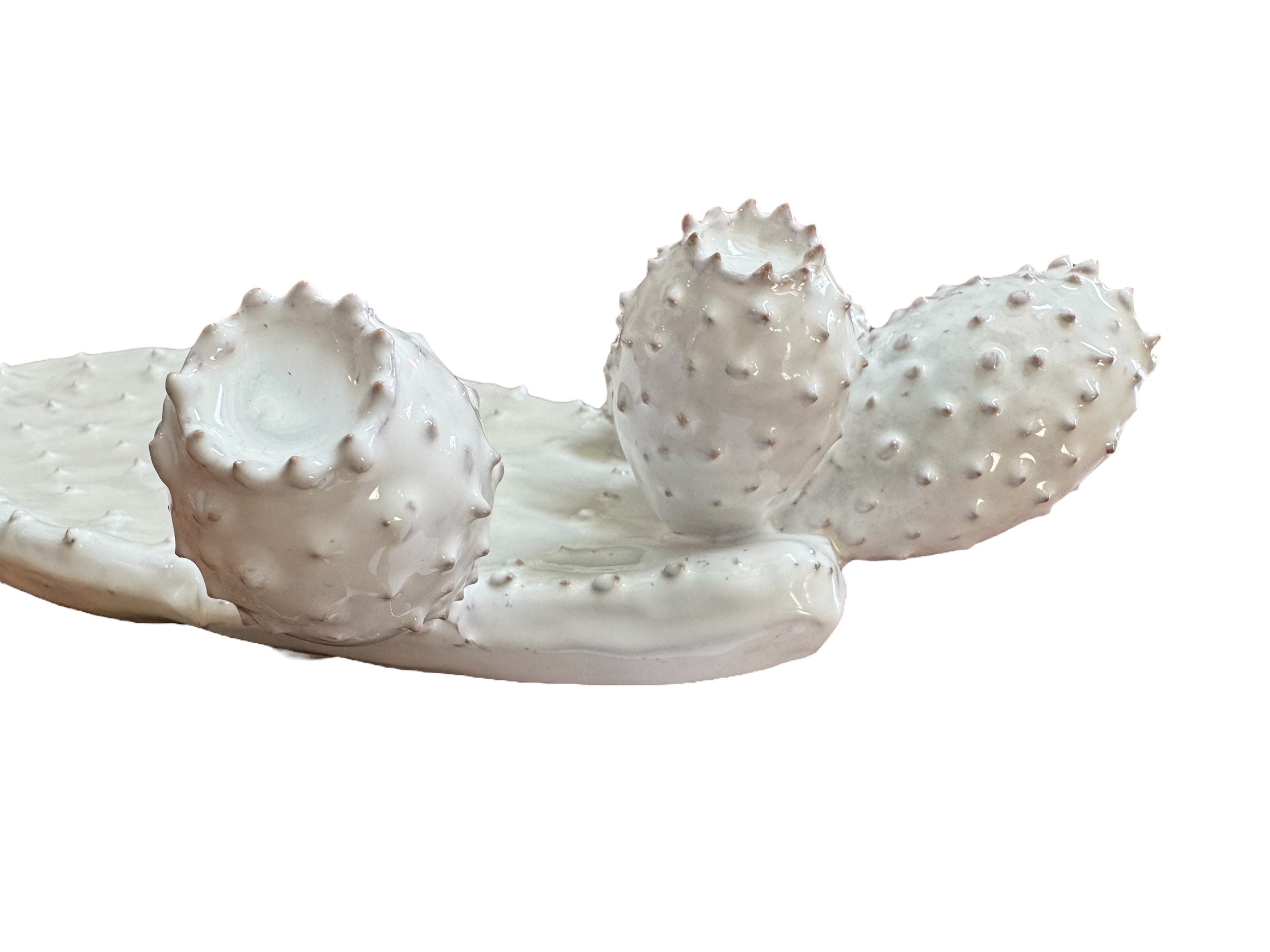 A white, glazed ceramic platter in the shape of a prickly pear cactus pad with attached prickly pear fruit. The surface has raised dots representing spines.