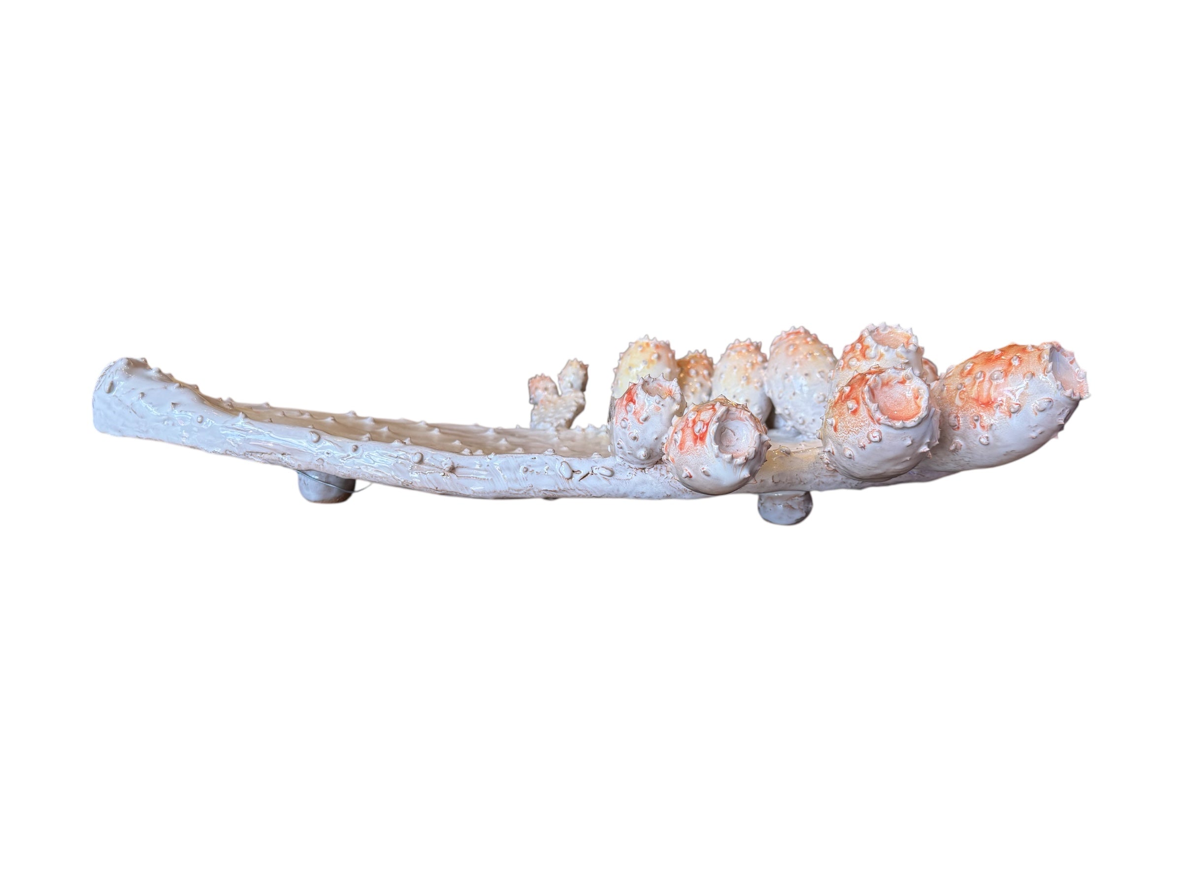 A white and orange, glazed ceramic platter in the shape of a prickly pear cactus pad with attached prickly pear fruit. The surface has raised dots representing spines.
