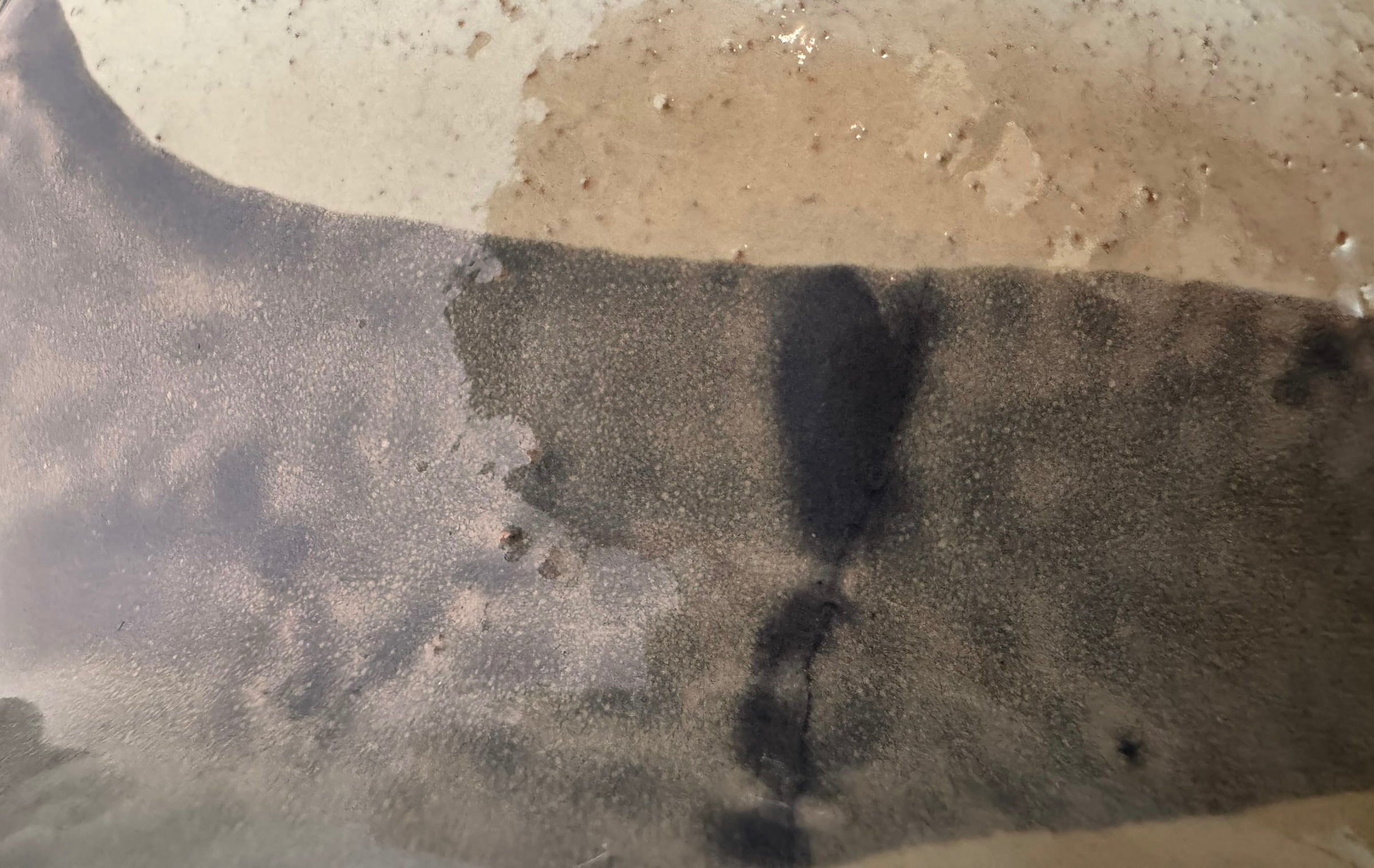 A ceramic sculpture of a bulldog's head by Enza Fasano. The piece features a glossy, glazed finish with a sophisticated color palette of muted greys, creams, and earthy brown tones arranged in bold, abstract striped patterns across the face and ears. The bulldog has characteristic folded ears, a prominent snout, and a soulful, slightly downturned expression. The sculpture is set against a clean, white background, highlighting its smooth texture and reflective surface.