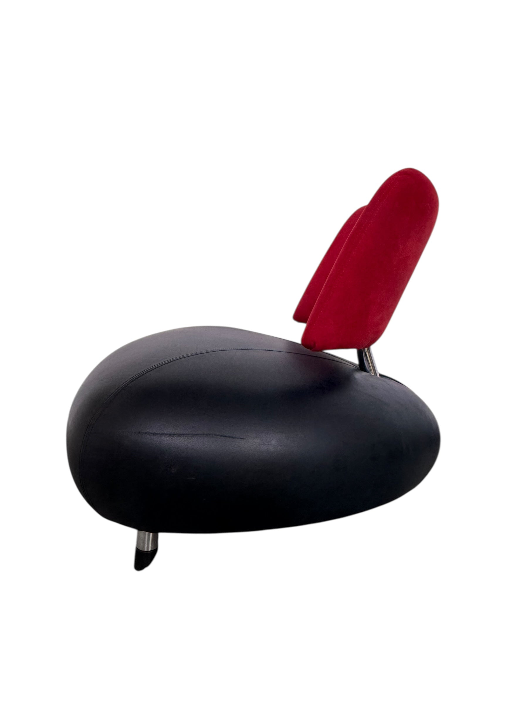 A Leolux Pallone armchair with a large, black, spherical leather seat and a smaller, red, curved leather backrest, supported by short metal legs.