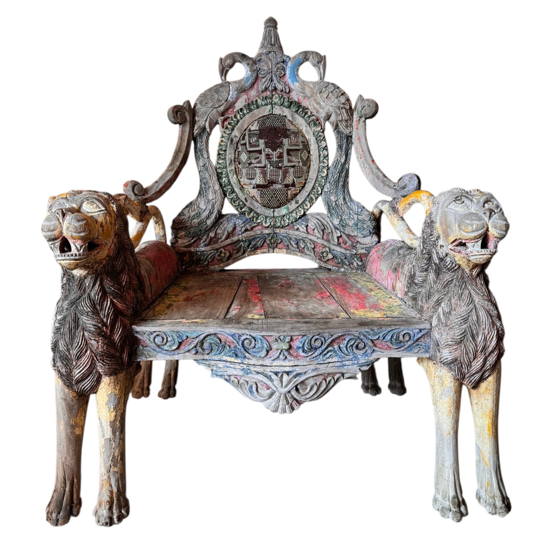 A pair of antique, heavily carved Anglo-Indian style throne chairs featuring lion figures as legs and arm supports, and peacock motifs on the backrests. The chairs have a distressed, multi-colored painted finish.