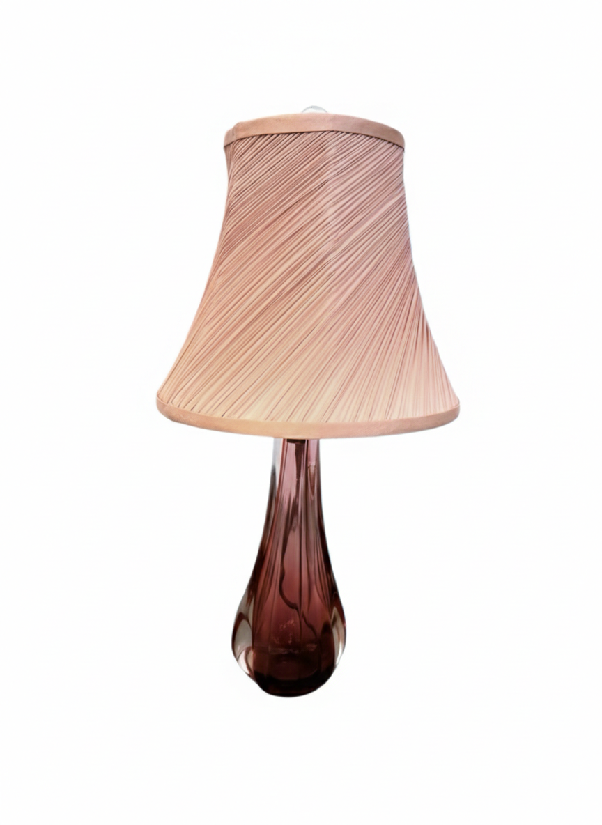A table lamp featuring a teardrop-shaped, reddish-purple glass base and a conical, pleated, light-pink fabric shade.