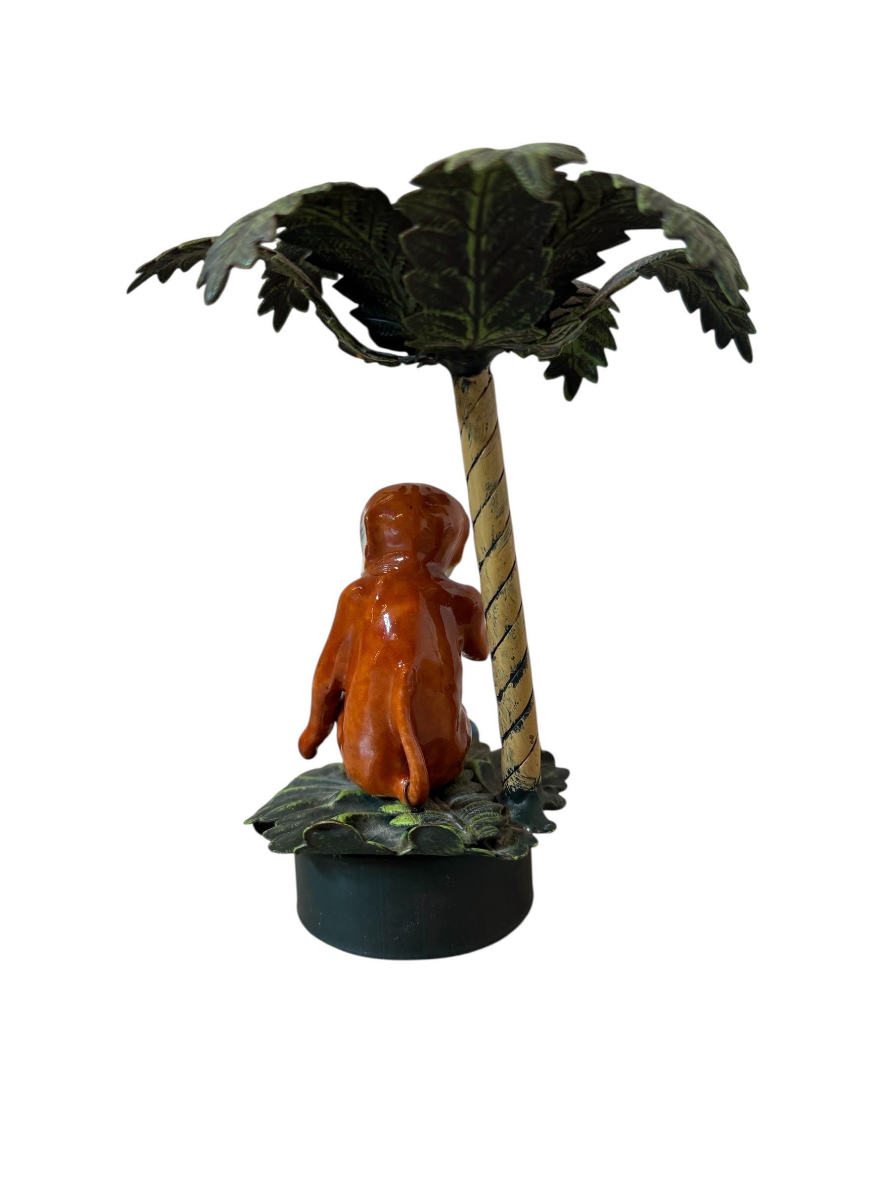 Small figurine of a child sitting under a palm tree on a white background