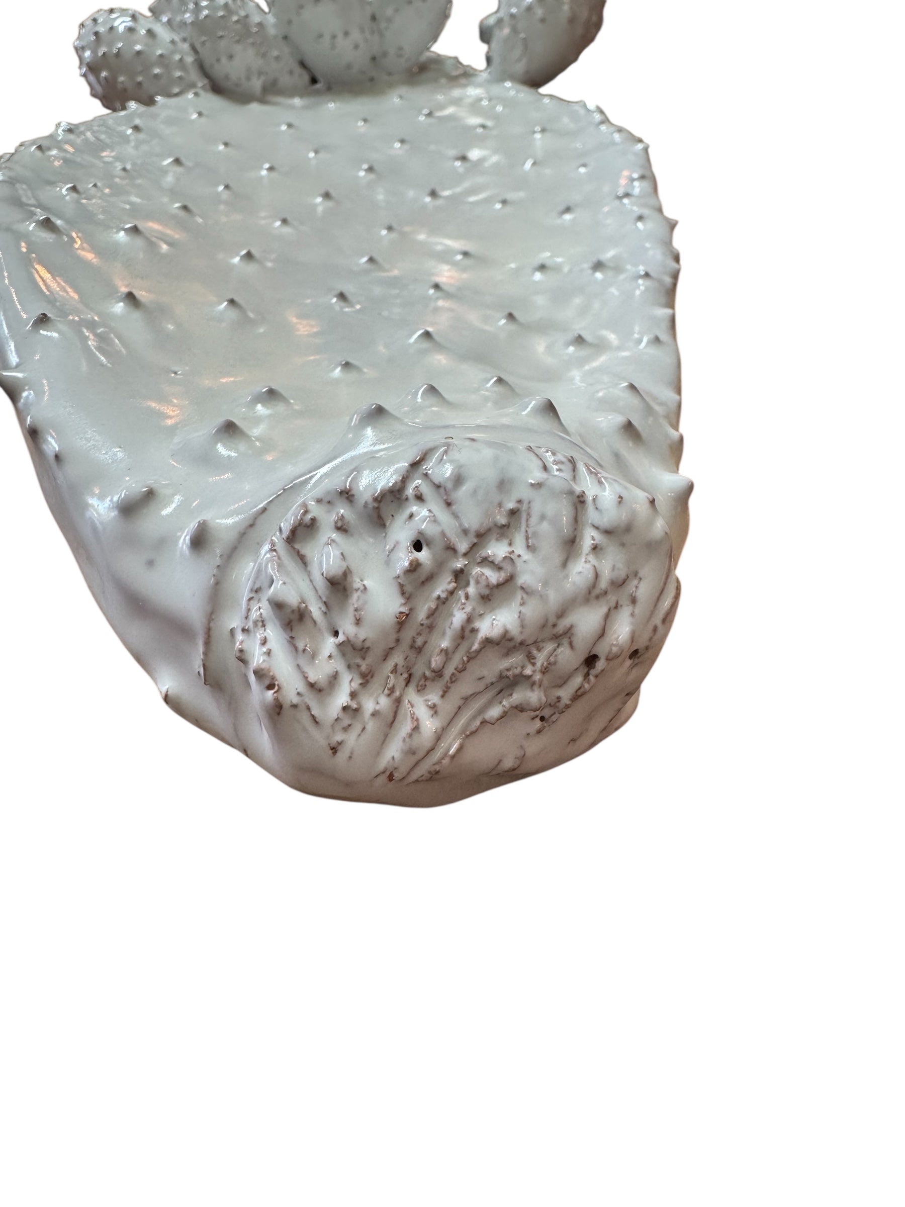 A white, glazed ceramic platter in the shape of a prickly pear cactus pad with attached prickly pear fruit. The surface has raised dots representing spines.