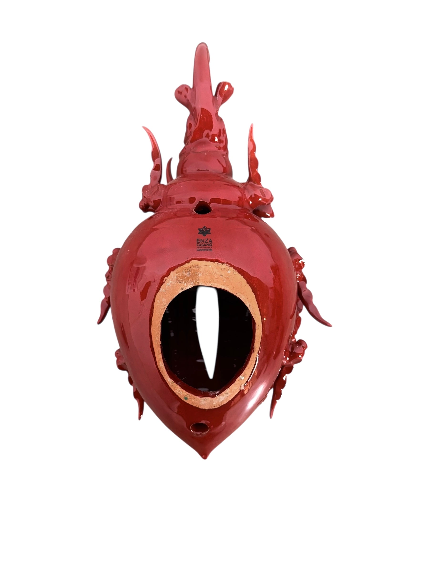 A vibrant, glossy red ceramic sculpture of a rhinoceros beetle by Enza Fasano. The piece features a highly reflective, deep crimson glaze that accentuates its smooth, rounded abdomen and the intricate, jagged textures of its head and horns.