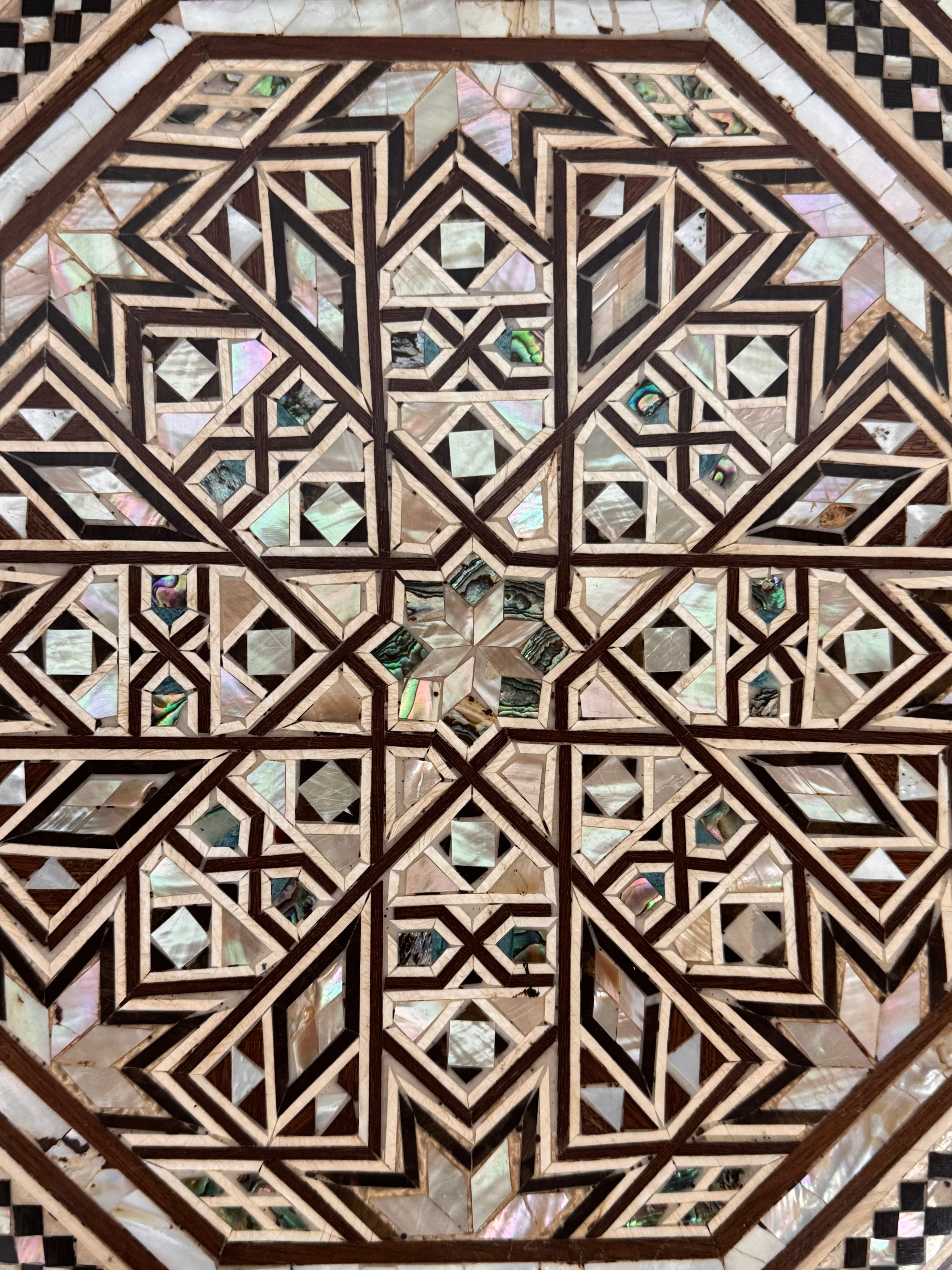 An ornate octagonal Syrian inlaid box, intricately decorated with geometric patterns made from dark wood, iridescent mother-of-pearl, vibrant abalone shell, and pale bone