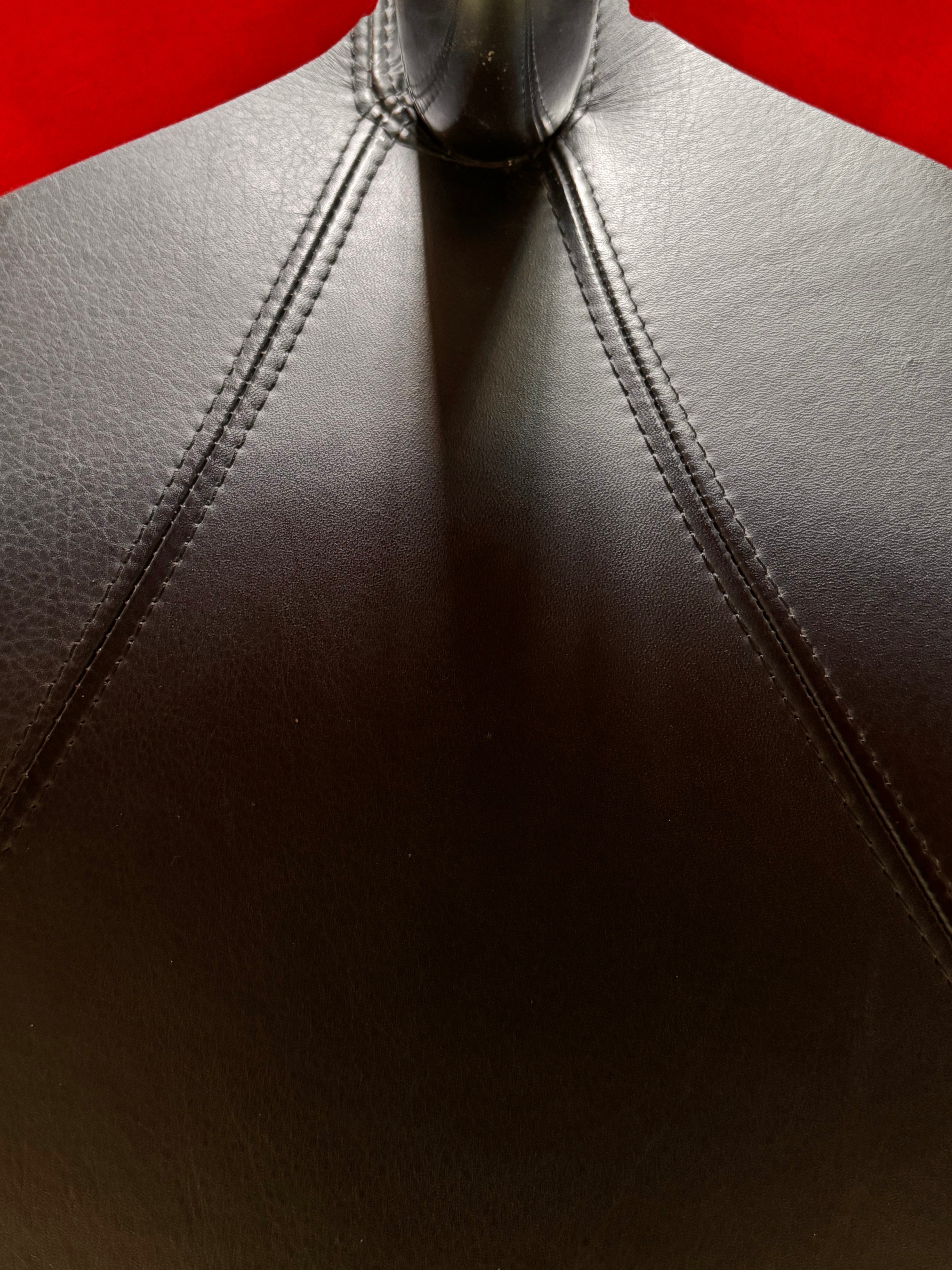 A Leolux Pallone armchair with a large, black, spherical leather seat and a smaller, red, curved leather backrest, supported by short metal legs.