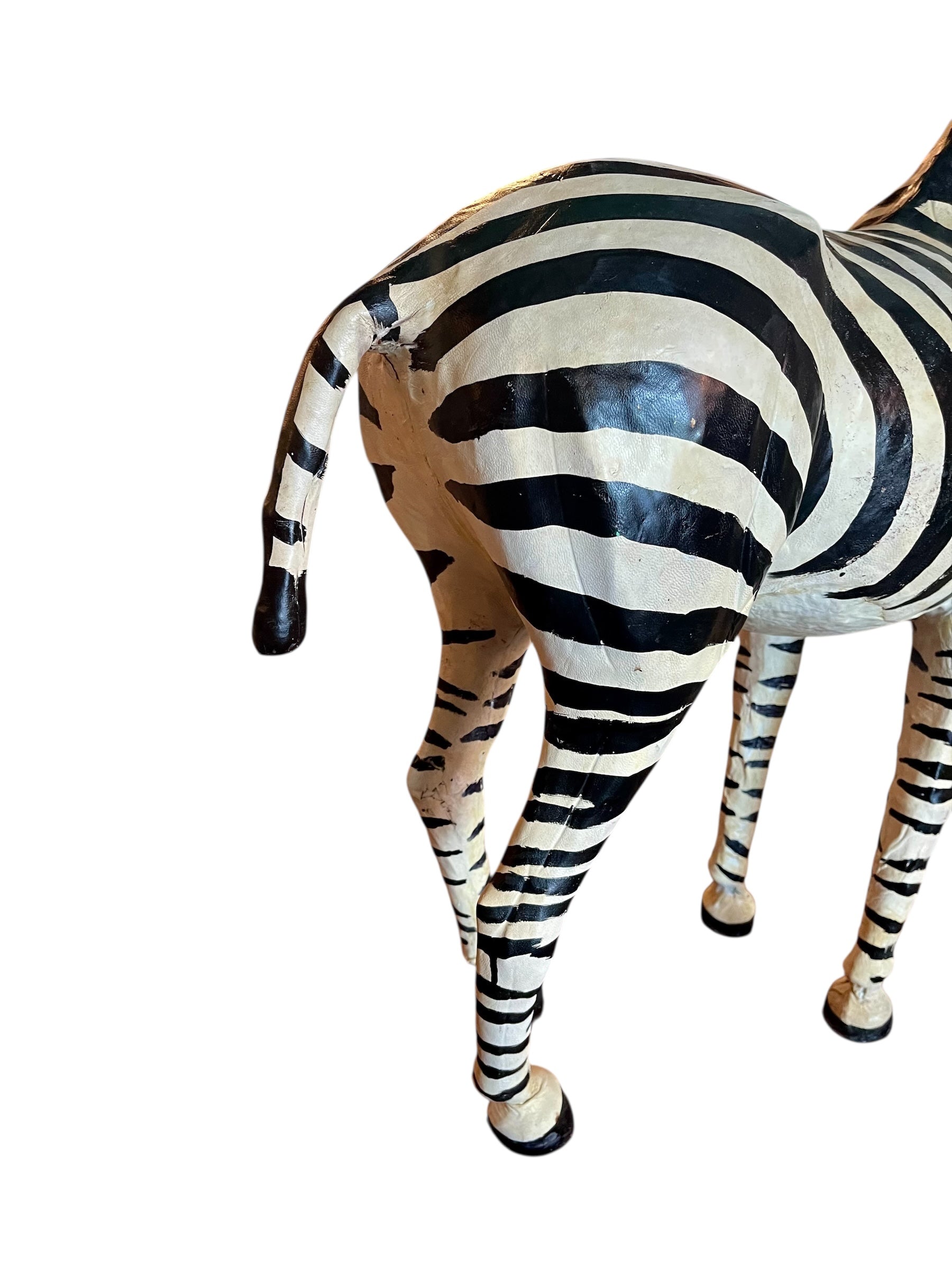 A full-length view of a standing zebra sculpture made from hand-painted leather. The sculpture features bold black and white stripes and shows signs of age, including slight yellowing and a tear on its leg.
Vintage
Antique
Art
Figurine
Decorative
Animal
Wear
Tear
Cream
Standing
Detailed
Full-length
Close-up
