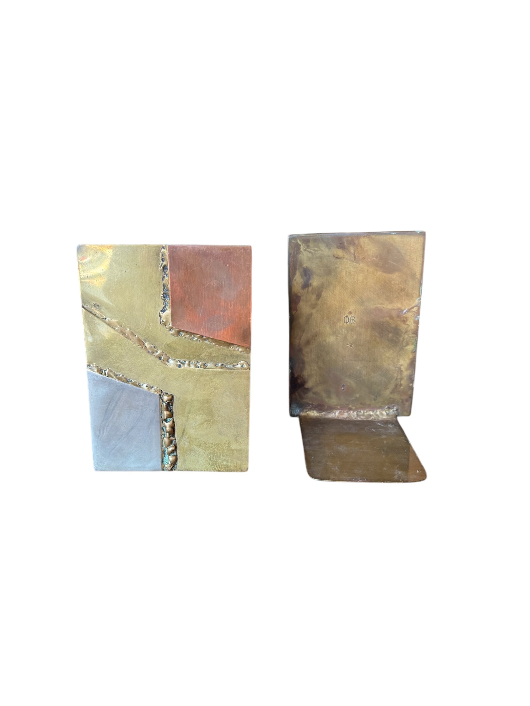 Close-up of two David Marshall Brutalist bookends. The bookends feature contrasting silver and bronze metal panels, separated by raised textured bronze seams. The bookends have a rough, geometric design.