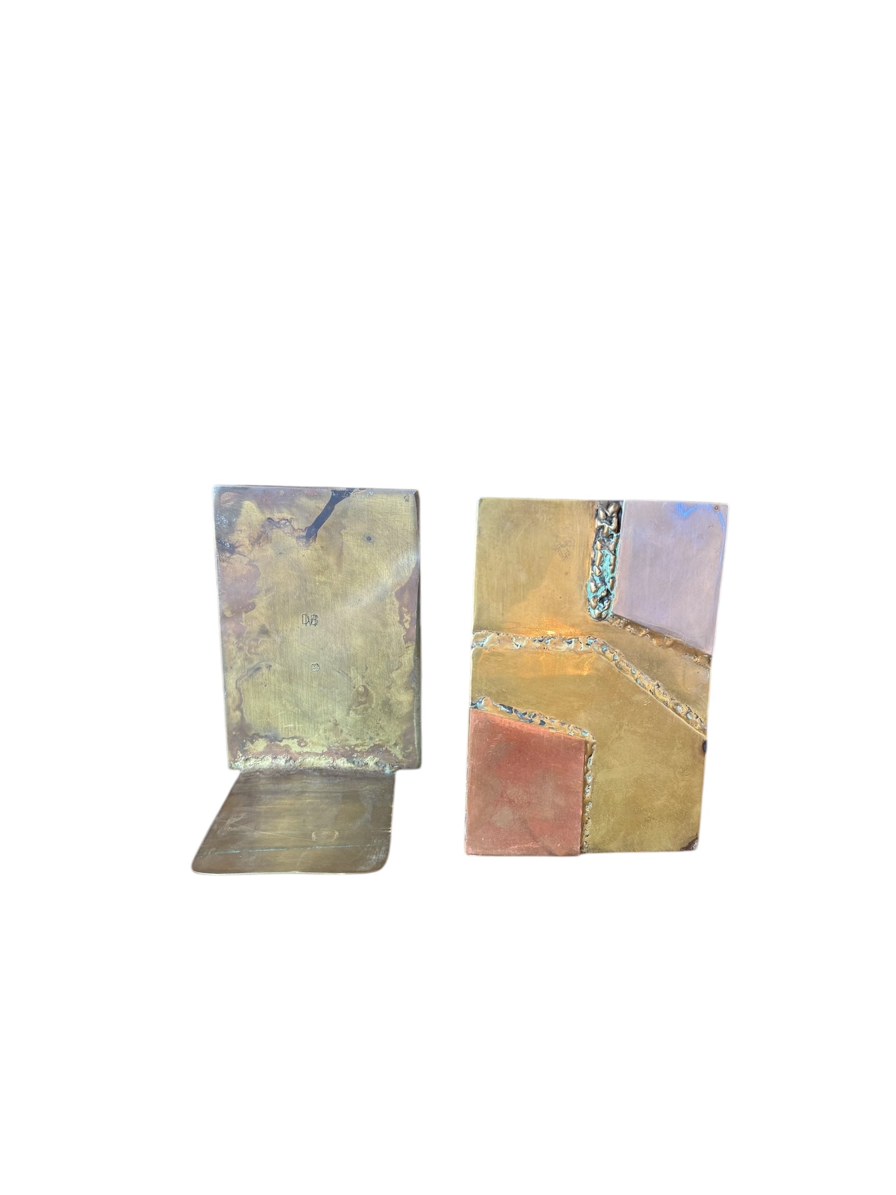 Close-up of two David Marshall Brutalist bookends. The bookends feature contrasting silver and bronze metal panels, separated by raised textured bronze seams. The bookends have a rough, geometric design.