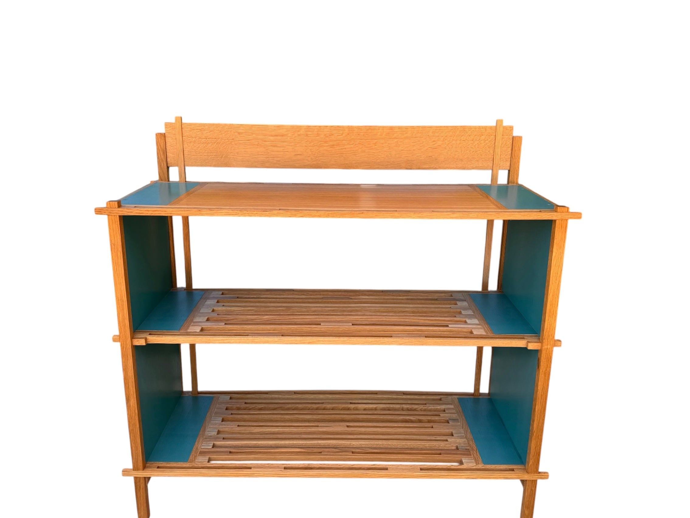 A three-tiered wooden shelving unit featuring a mix of light oak and teal-colored panels. The piece has an open, structural design with visible joinery, vertical supports that extend past the top shelf, and a horizontal backrest at the top. The middle and bottom shelves feature slatted wood center sections flanked by solid teal panels, while the top surface is primarily solid wood with teal accents at the edges.