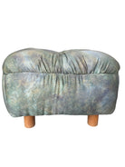 A vintage 1990s ottoman with a mottled green, blue, and gold upholstery, tufted top, and wooden feet.