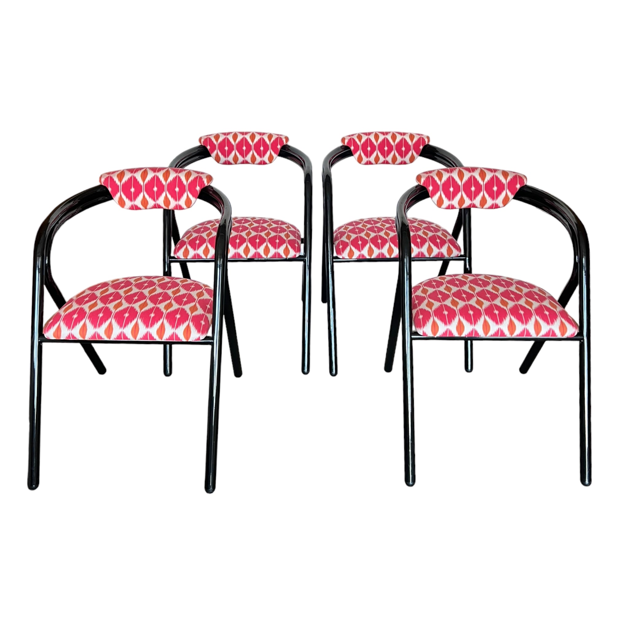 A set of four post modern chairs with black frames and seat cushions upholstered in a geometric pattern of pink, orange, and white.