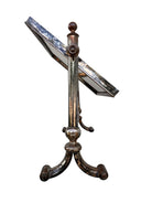 The antique Chevalier Mirror features a rectangular swing frame supported by two turned posts on decorative trestle feet. The mirror stands on four scrolled feet and features its original tarnished, silvered finish. The front of the mirror reflects a bright blue sky with wispy white clouds. The original dark brown backing is still attached to the frame.