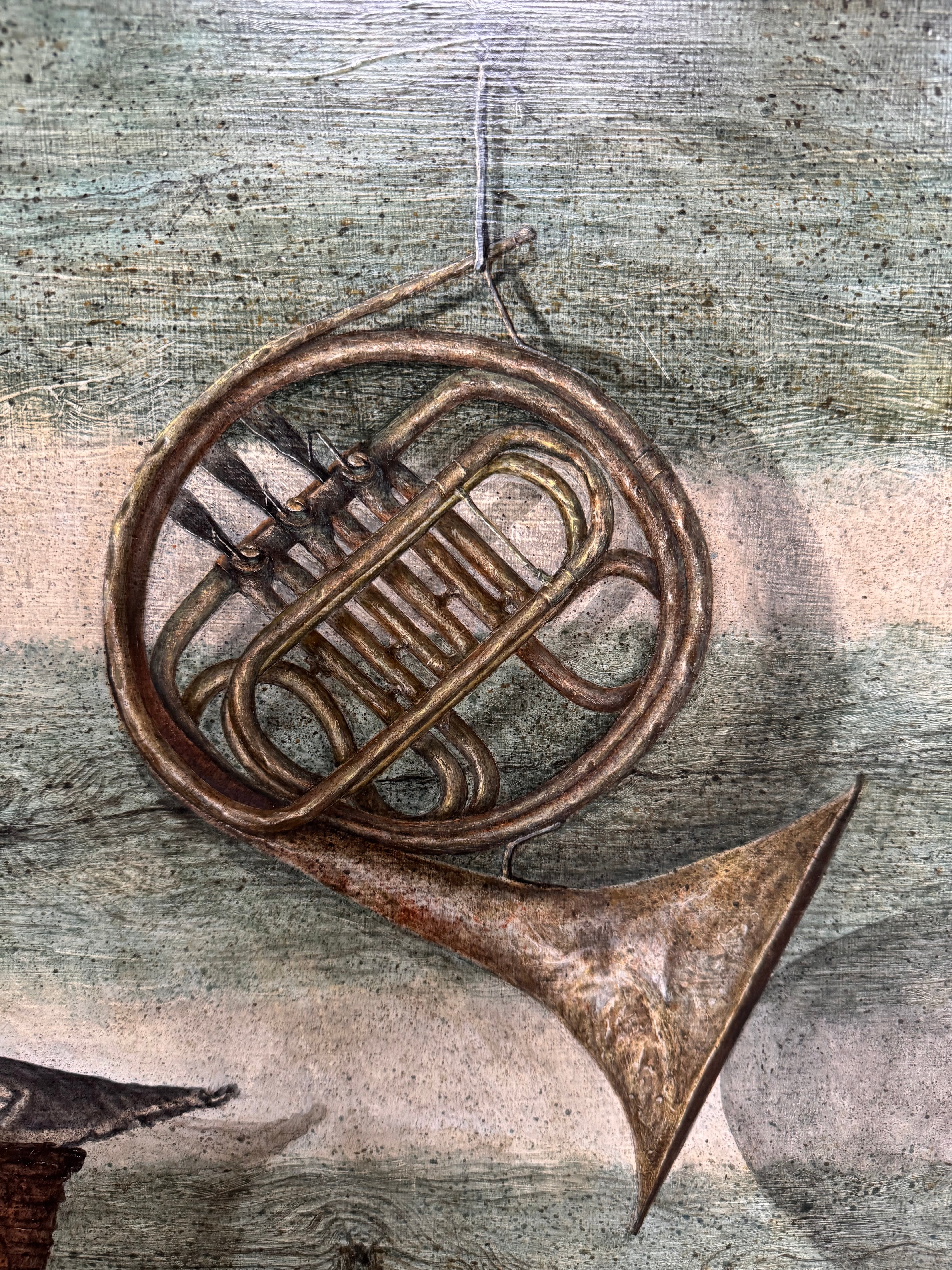 A realistic painting of a rustic interior scene by Travis Whitfield. A duck sits inside a woven basket on a dark wooden table with a single drawer. A French horn hangs on the light blue and white log wall behind the table. A multi-pane window on the left side of the painting shows an outdoor view. 