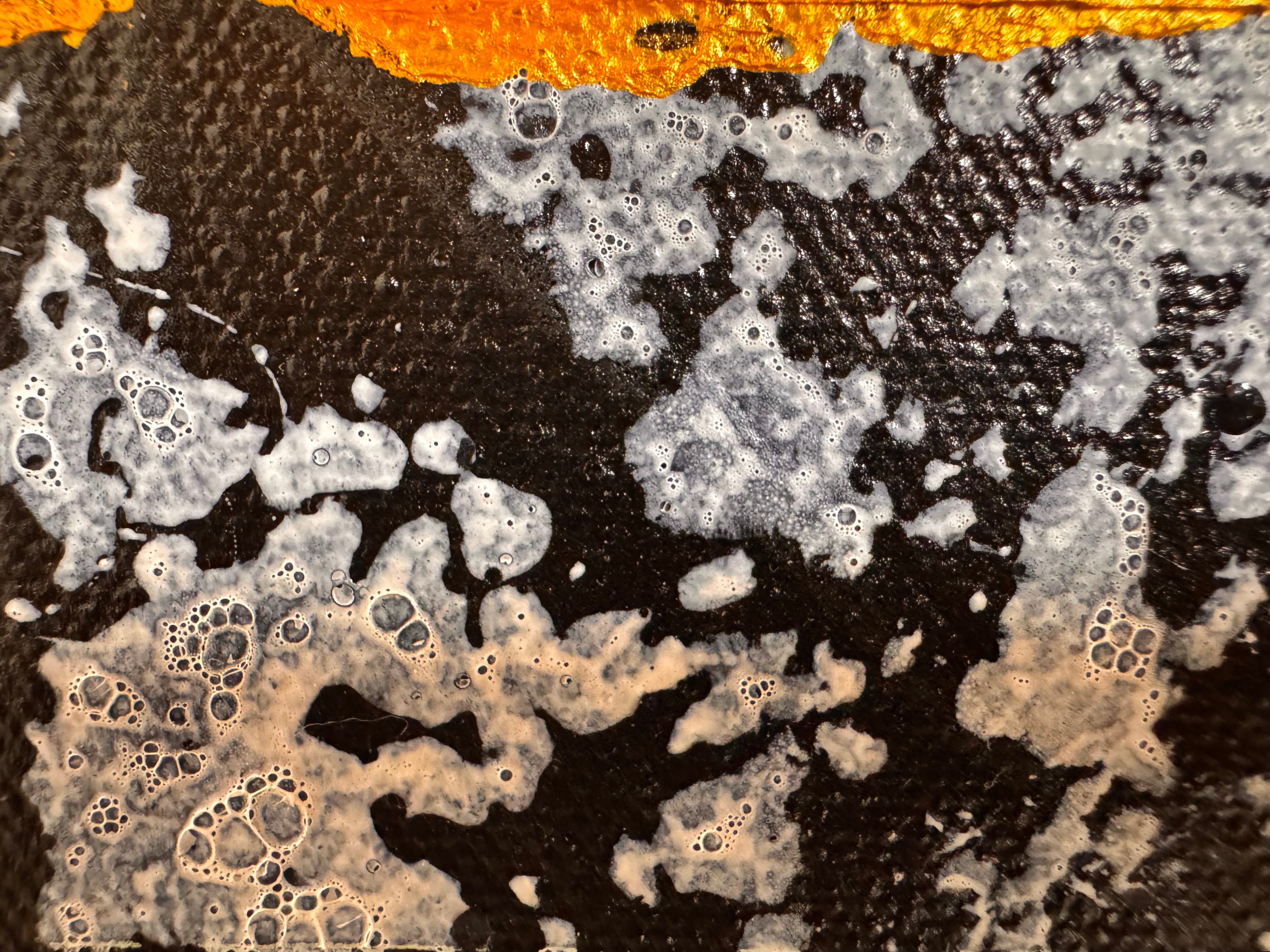 An abstract, vertical-oriented canvas painting featuring a dark background layered with highly textured, horizontal bands. The composition alternates between solid black strips and dense, speckled white-and-grey patterns that resemble static or stone texture. Splattered across the surface are energetic drips, lines, and splotches of bright yellow, stark white, and grey paint, creating a chaotic yet rhythmic sense of movement overlaying the geometric structure underneath.