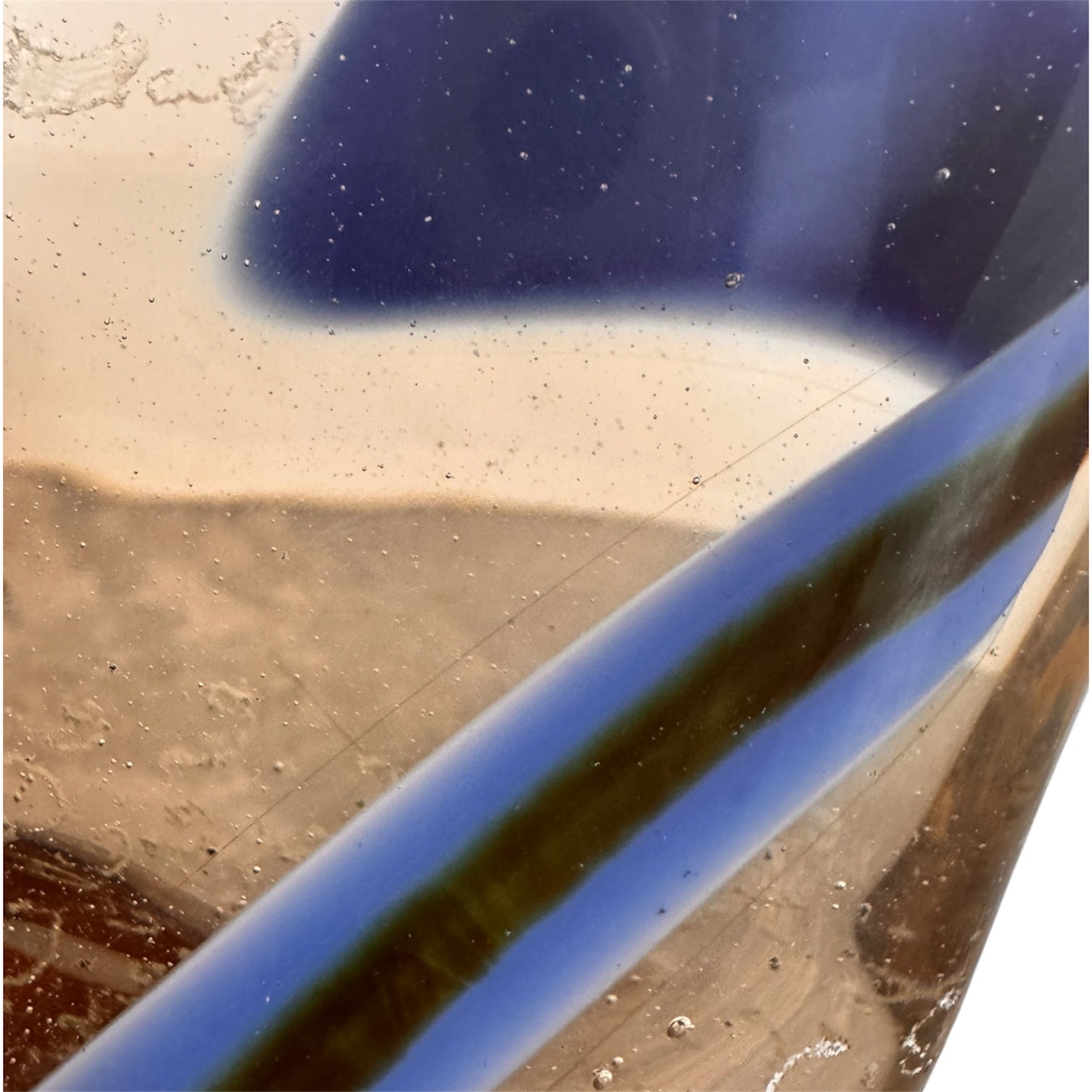 An asymmetrical Murano art glass sculpture with a heavy, biomorphic form. The piece is composed of thick, translucent smoky-amber glass with abstract, fluid bands of deep blue and dark brown swirling throughout the upper rim and sides. A dense pattern of tiny, controlled air bubbles is suspended inside the glass, concentrating heavily near the thick, solid amber base.