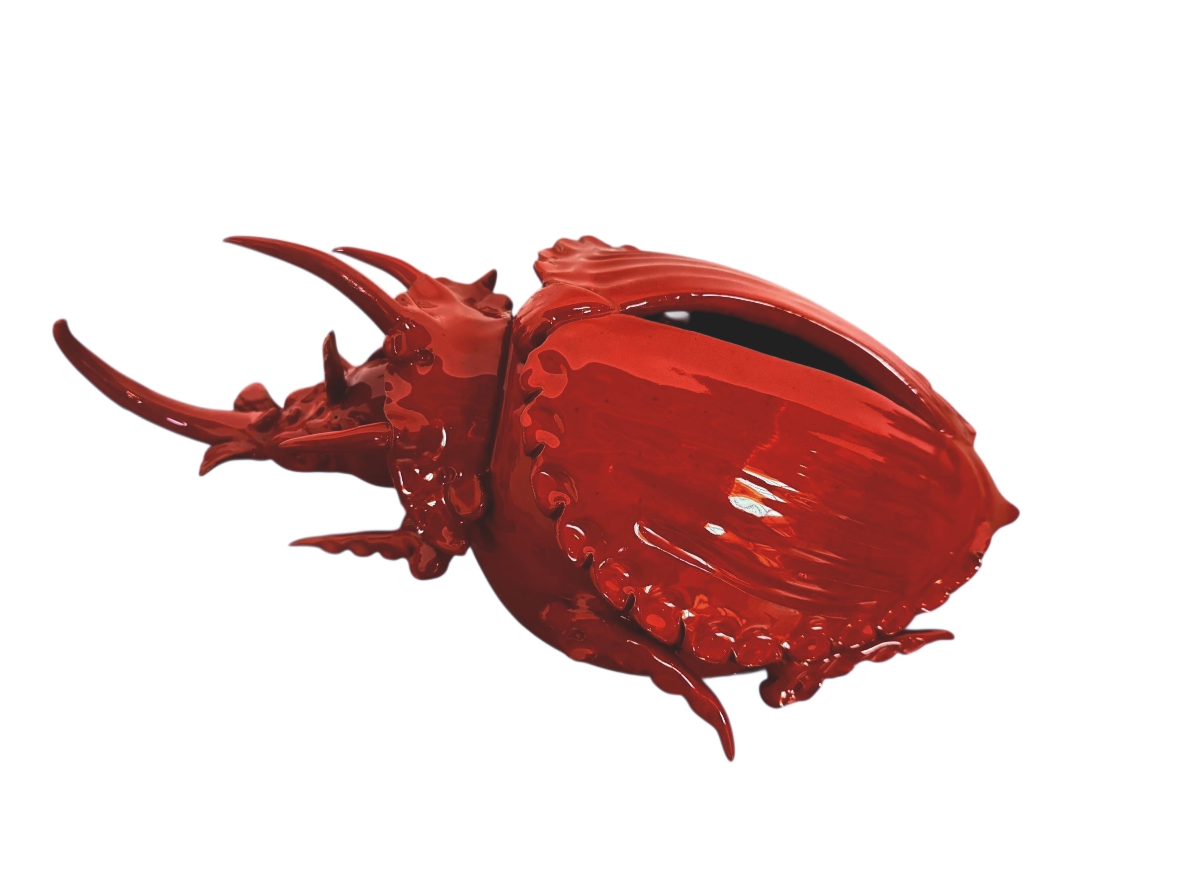A vibrant, glossy red ceramic sculpture of a rhinoceros beetle by Enza Fasano. The piece features a highly reflective, deep crimson glaze that accentuates its smooth, rounded abdomen and the intricate, jagged textures of its head and horns.
