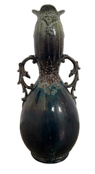 An ornate, dark glazed ceramic Art Nouveau vase with two handles and raised floral designs in yellow, purple, and green.