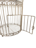 A single, white or cream-colored, decorative wrought iron bird cage with a hinged door and a hanging loop at the top. The cage has a vintage or antique style 