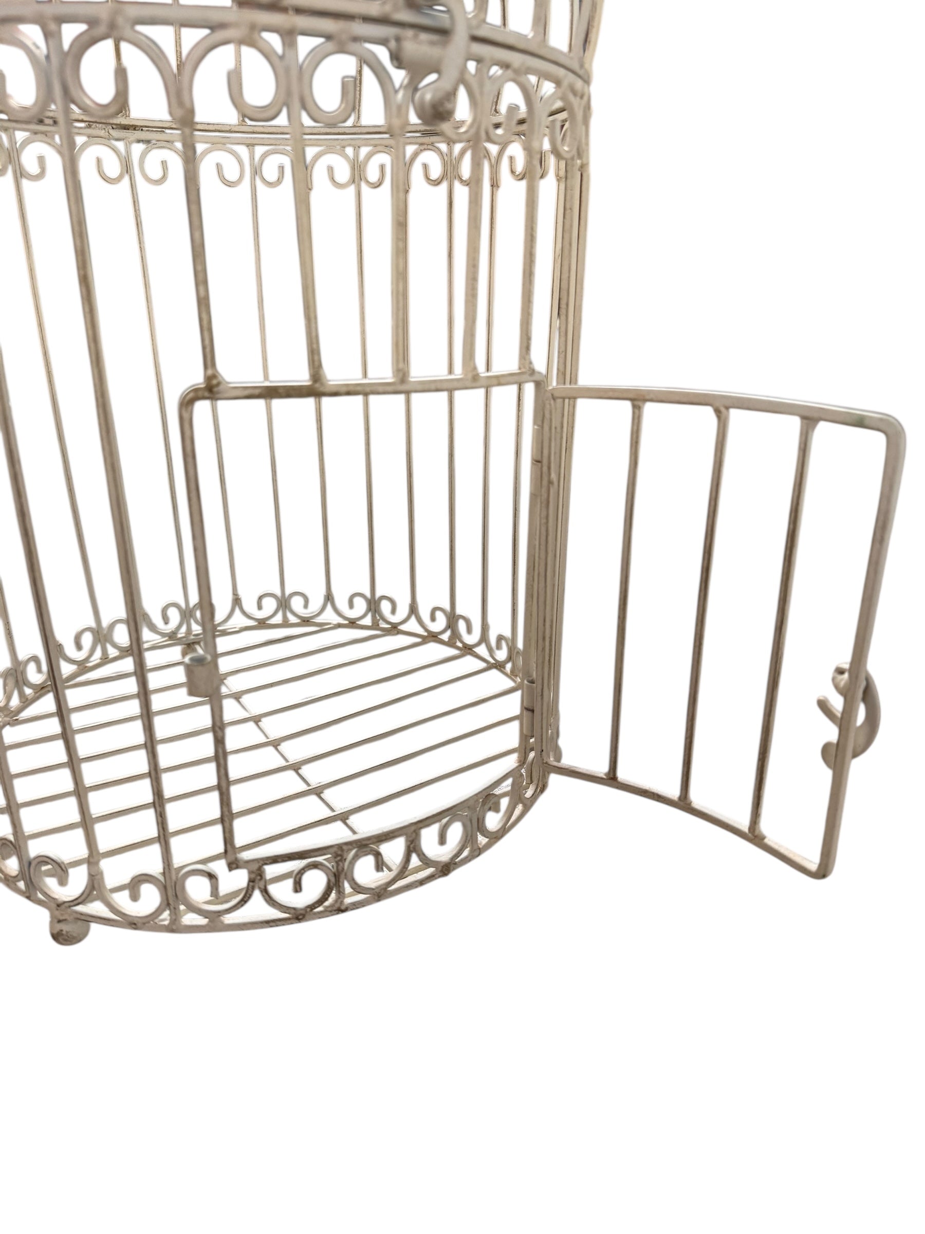 A single, white or cream-colored, decorative wrought iron bird cage with a hinged door and a hanging loop at the top. The cage has a vintage or antique style 