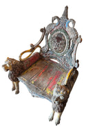A pair of antique, heavily carved Anglo-Indian style throne chairs featuring lion figures as legs and arm supports, and peacock motifs on the backrests. The chairs have a distressed, multi-colored painted finish.