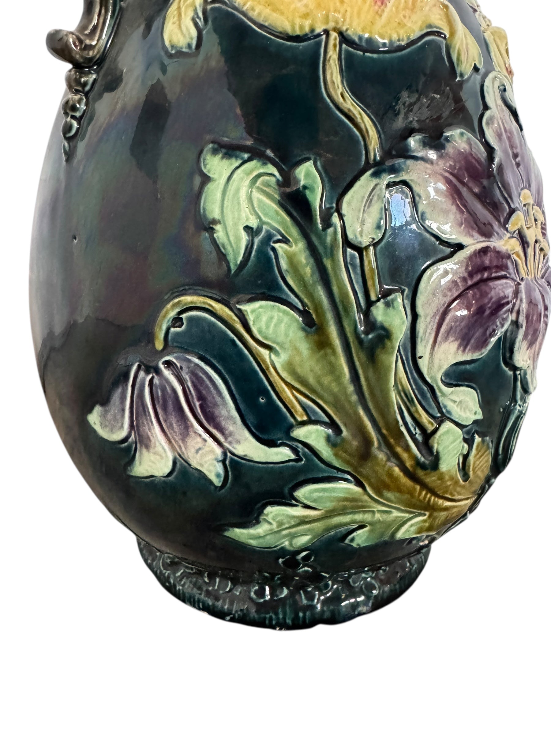 An ornate, dark glazed ceramic Art Nouveau vase with two handles and raised floral designs in yellow, purple, and green.