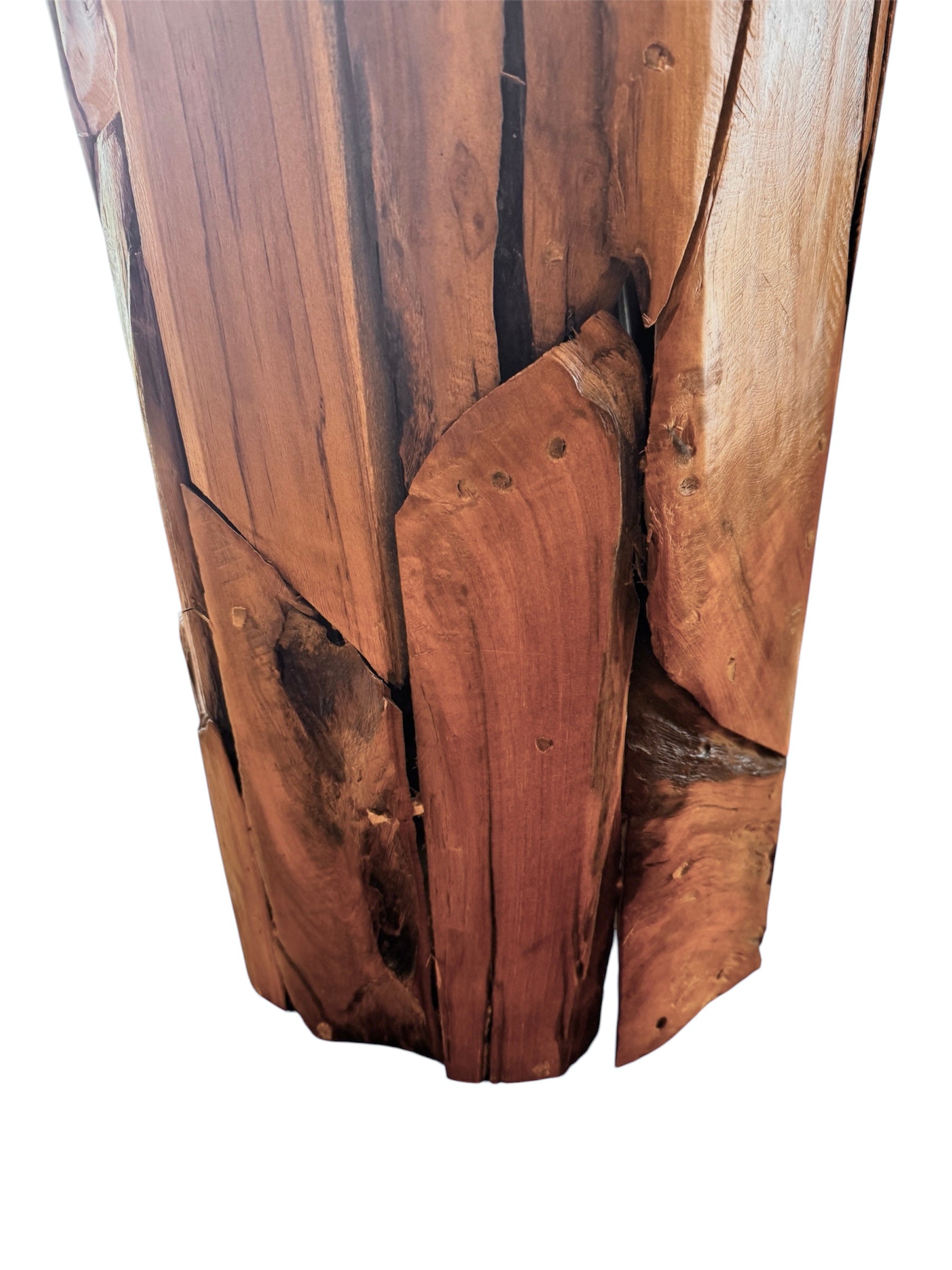 Two table lamps made from repurposed teak wood vases. The bases are tall and tapered, featuring a rugged, mosaic-like texture composed of various pieces of dark, polished teak wood with visible natural grain and crevices. Each lamp is topped with a large, warm-toned conical shade that is currently wrapped in protective clear plastic, emitting a soft, golden glow. The lamps are positioned on a clean white surface against a neutral background.
