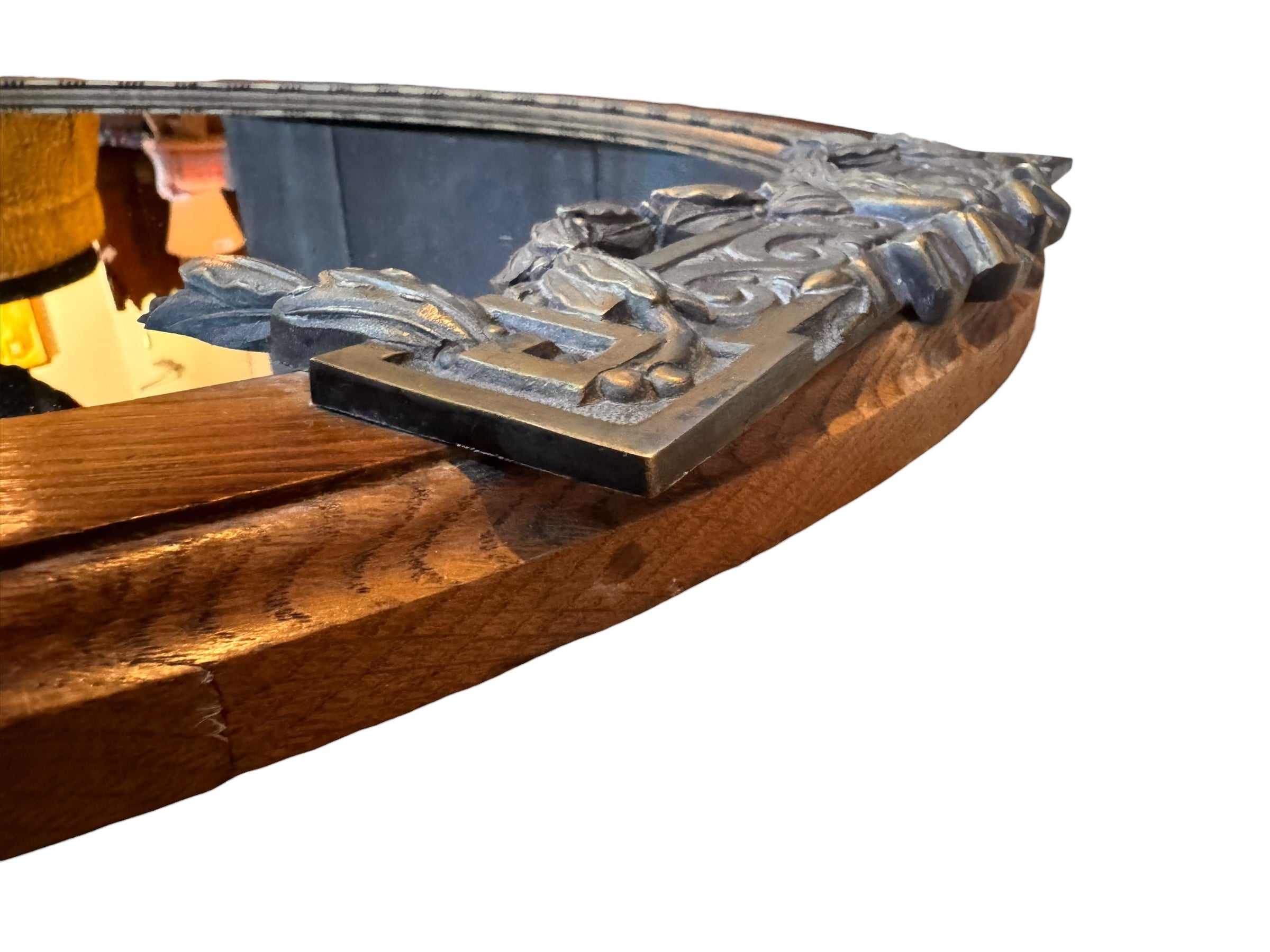 An oval-shaped mirror featuring a wooden frame and an ornate metal crest at the top.