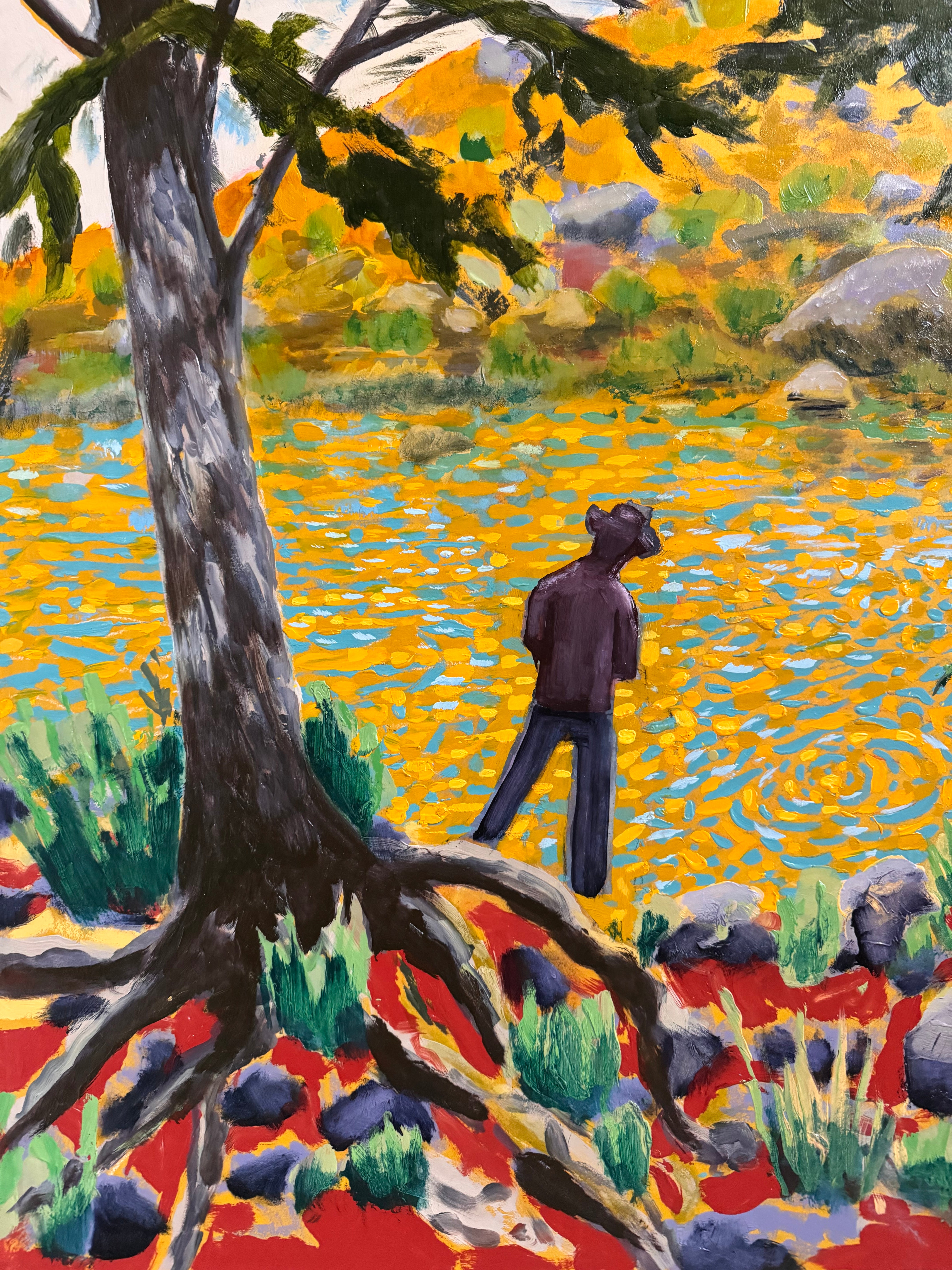 A vibrantly colored landscape painting titled 'Perdernales Falls Fisherman,' featuring two large trees with prominent exposed roots framing a body of water. A lone figure, a fisherman, stands by the water in the middle ground. The painting uses bold strokes of yellow, green, red, and blue, and is enclosed in a rustic dark wooden frame with a light-colored inner mat.