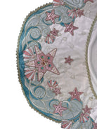 A round, cream-colored tablecloth featuring a dramatic, scalloped border shaped like six large flower petals. The border is intricately embroidered with a coastal motif including pink starfish, seashells, and teal-blue swirling waves. Gold beaded accents line the inner circular seam and the outer edges.
A long, narrow cream runner with matching scalloped, wavy edges. It is adorned with the same nautical embroidery of pink starfish and seashells scattered across the center and concentrated along the edge.