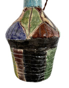 A hand-crafted ceramic table lamp featuring a vibrant, multi-colored base and a sleek black shade. The base is an upcycled artisan vase with a textured, hand-thrown appearance, decorated with geometric panels in shades of mustard yellow, forest green, cobalt blue, and burgundy, separated by thick black outlines. The lamp is topped with a minimalist, black tapered drum shade that provides a sharp contrast to the colorful, eclectic pottery below.
