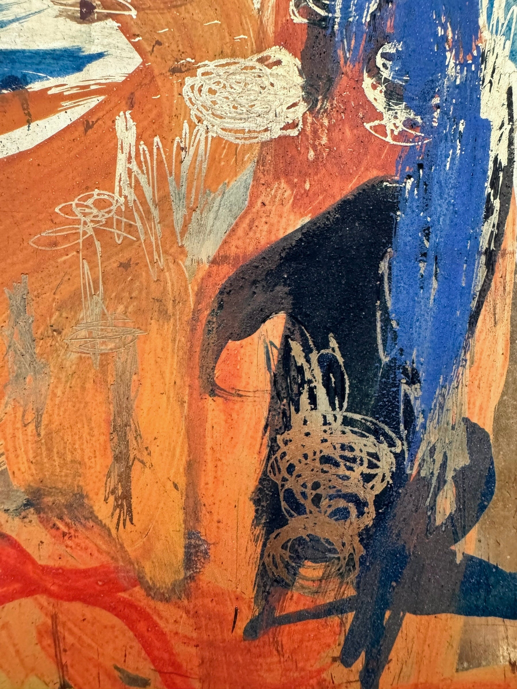 A vertical abstract painting on a shimmering gold-leaf background. The piece is filled with energetic, calligraphic scribbles and fluid shapes in vibrant orange, deep teal, and touches of red. The brushwork varies from thick, opaque strokes to thin, wiry lines that dance across the reflective surface. The composition feels organic and chaotic, like a dense thicket or a fire.